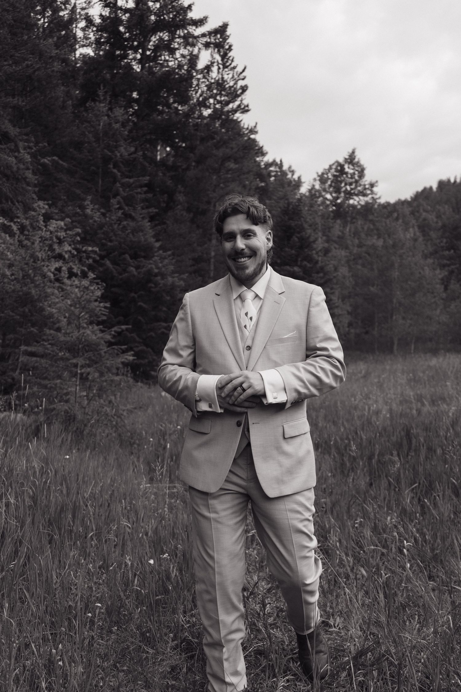 Handsome groom in light gray suit smiling in black and white forest wedding portrait.
