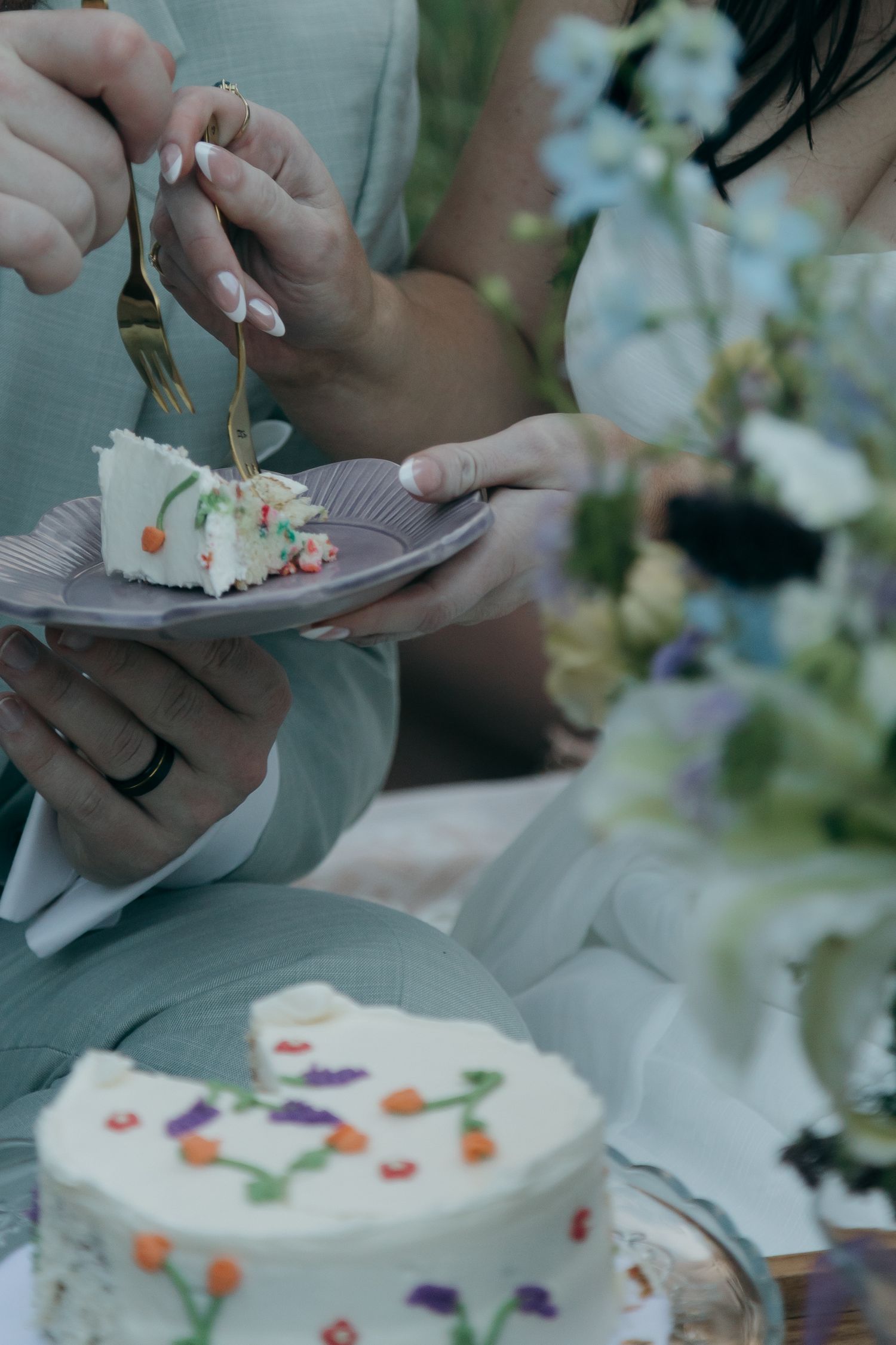 Bride and groom sharing wedding cake with white frosting and floral decorations at an outdoor garden celebration.