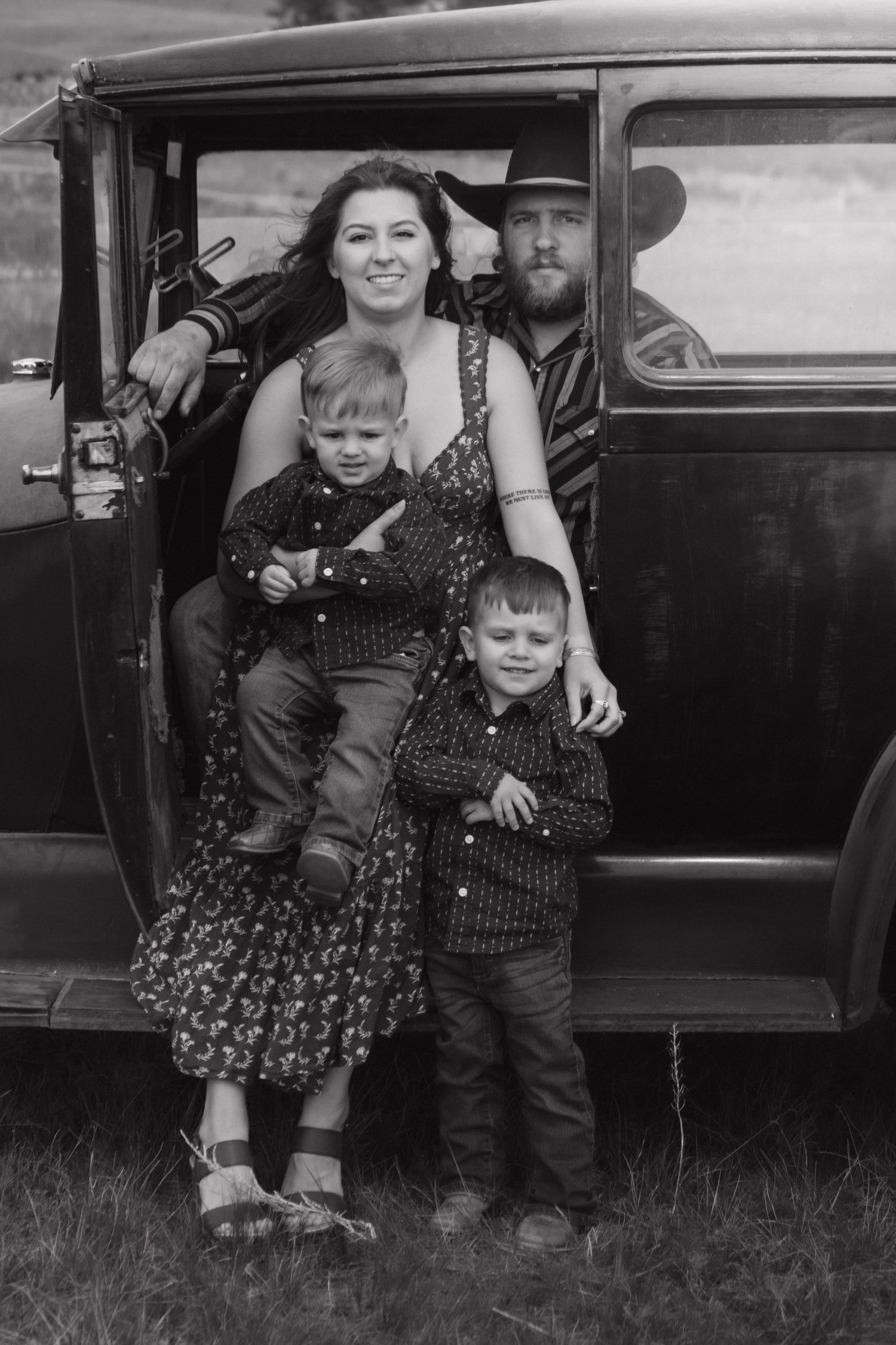Black and white portrait of a family grouped together by their vintage car.