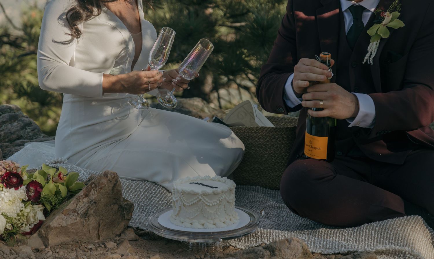 Bride and groom celebrate with champagne and wedding cake during intimate mountain elopement picnic.