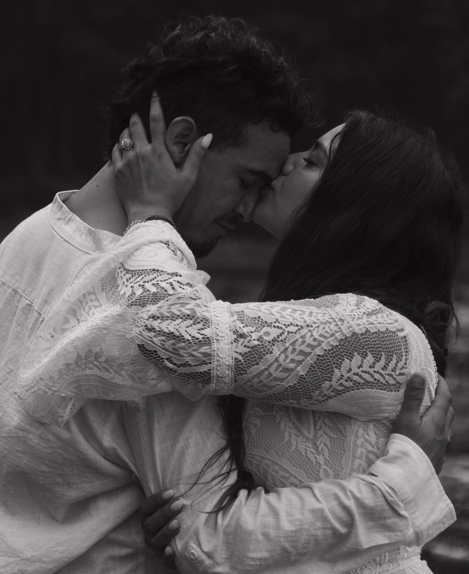 Black and white photo of couple sharing a passionate kiss, bride in lace dress holding groom's face.