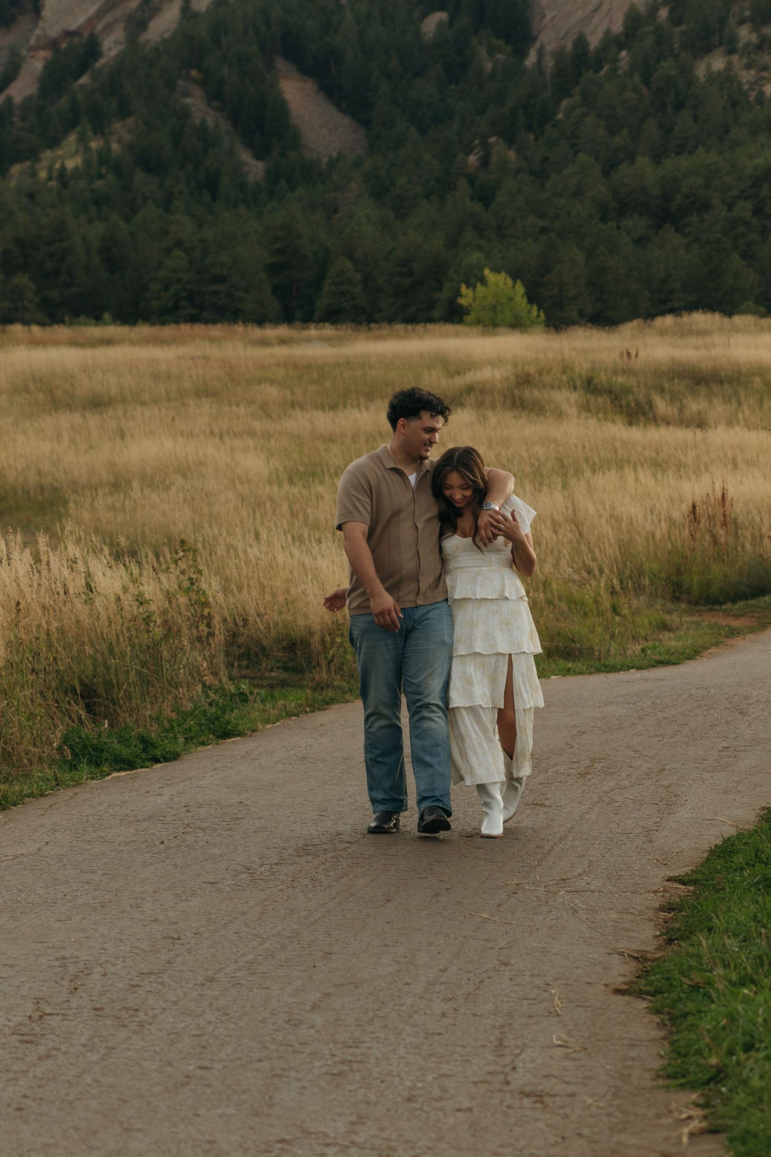 Happy couple walking arm in arm along a path through a scenic golden meadow at sunset.