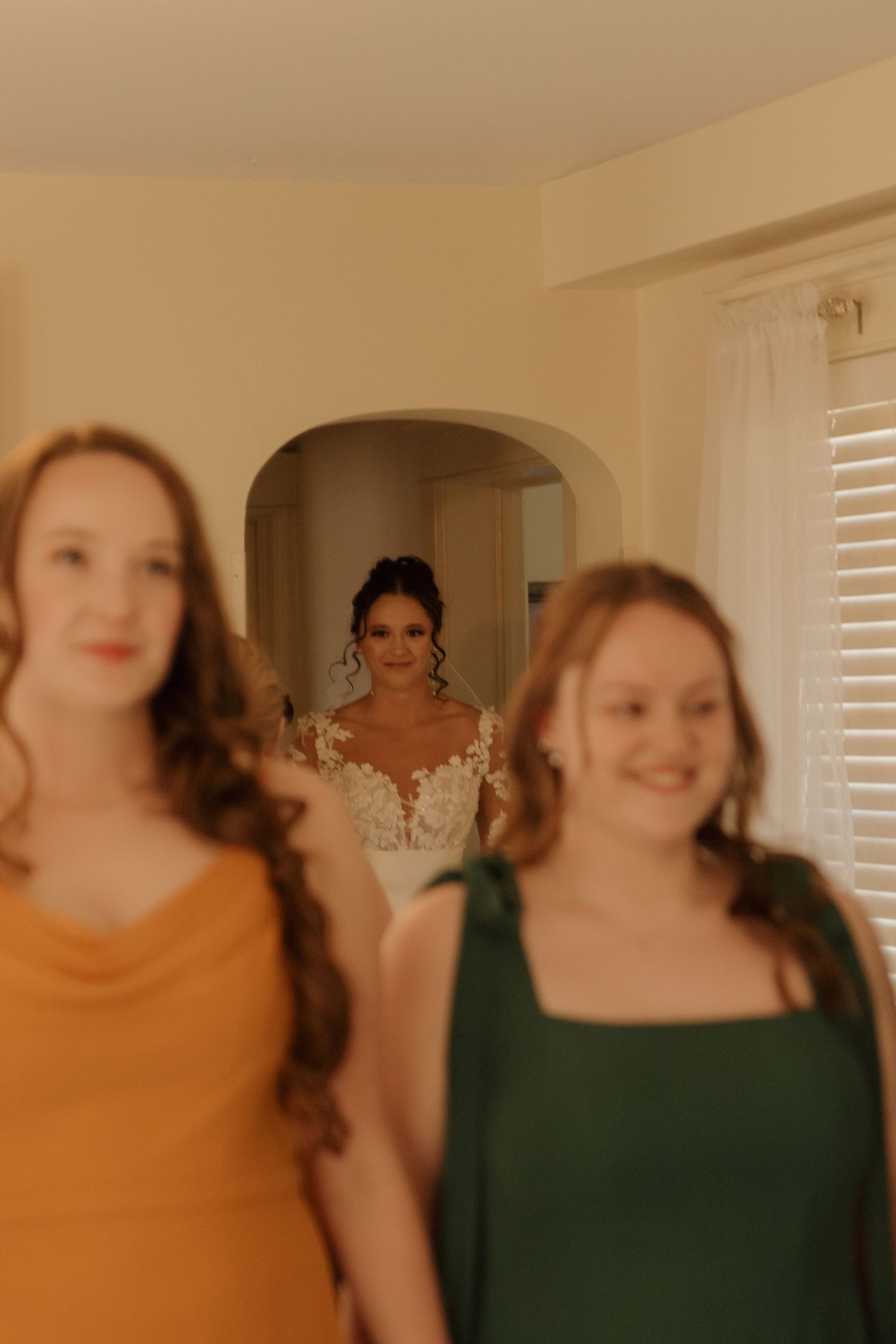 Bridesmaids in warm-toned dresses getting ready in a sunlit room.