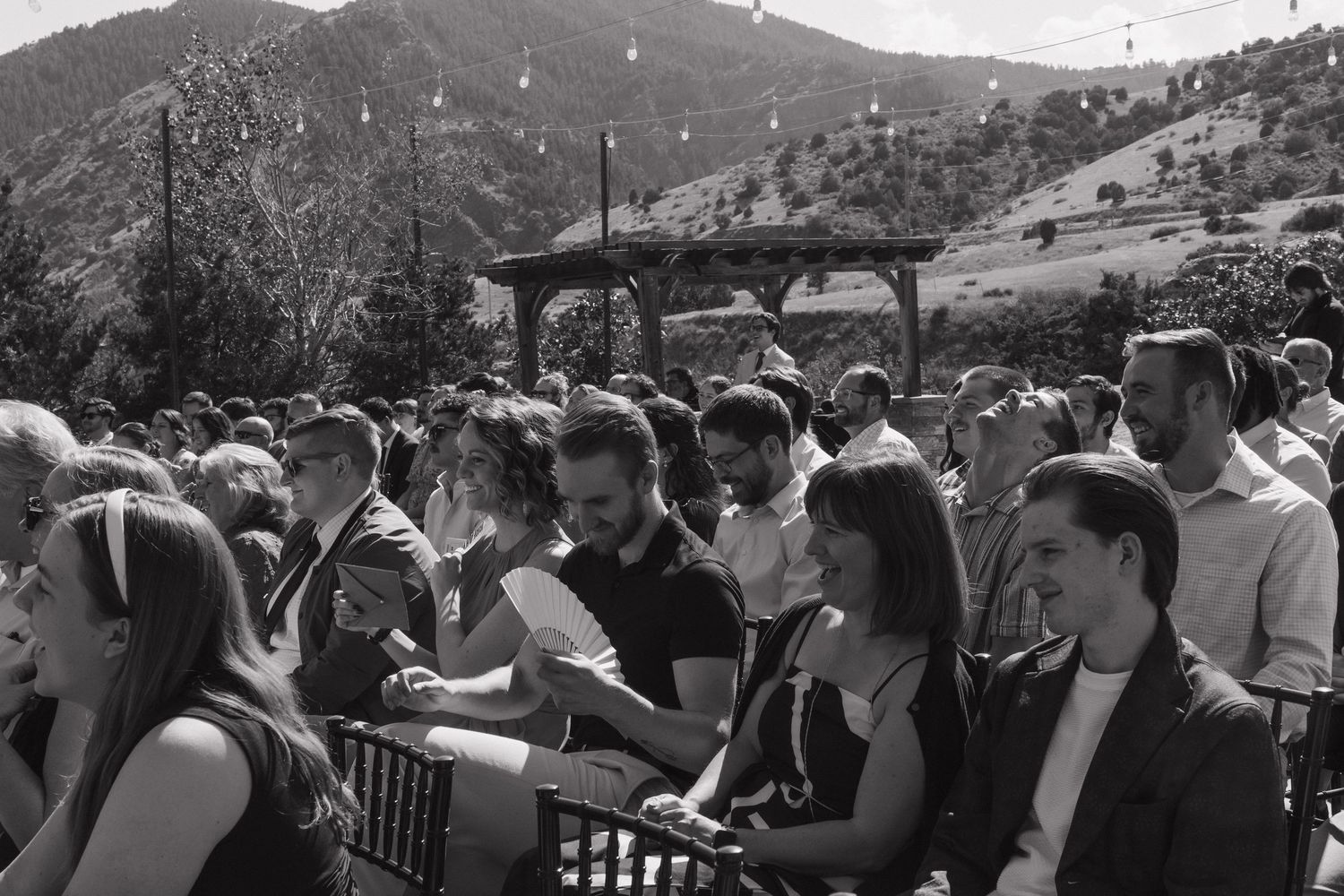 Wedding guests seated outdoors with mountains visible in the background.
