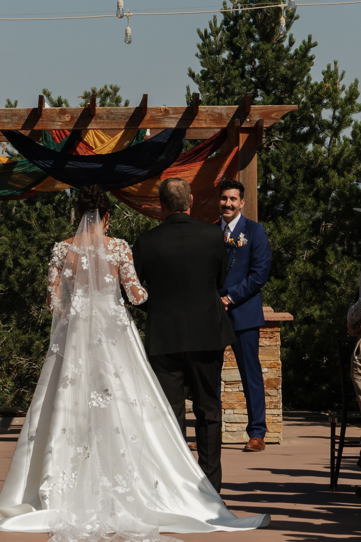 An elegant white wedding dress with lace details and long train stands in an outdoor ceremony space.