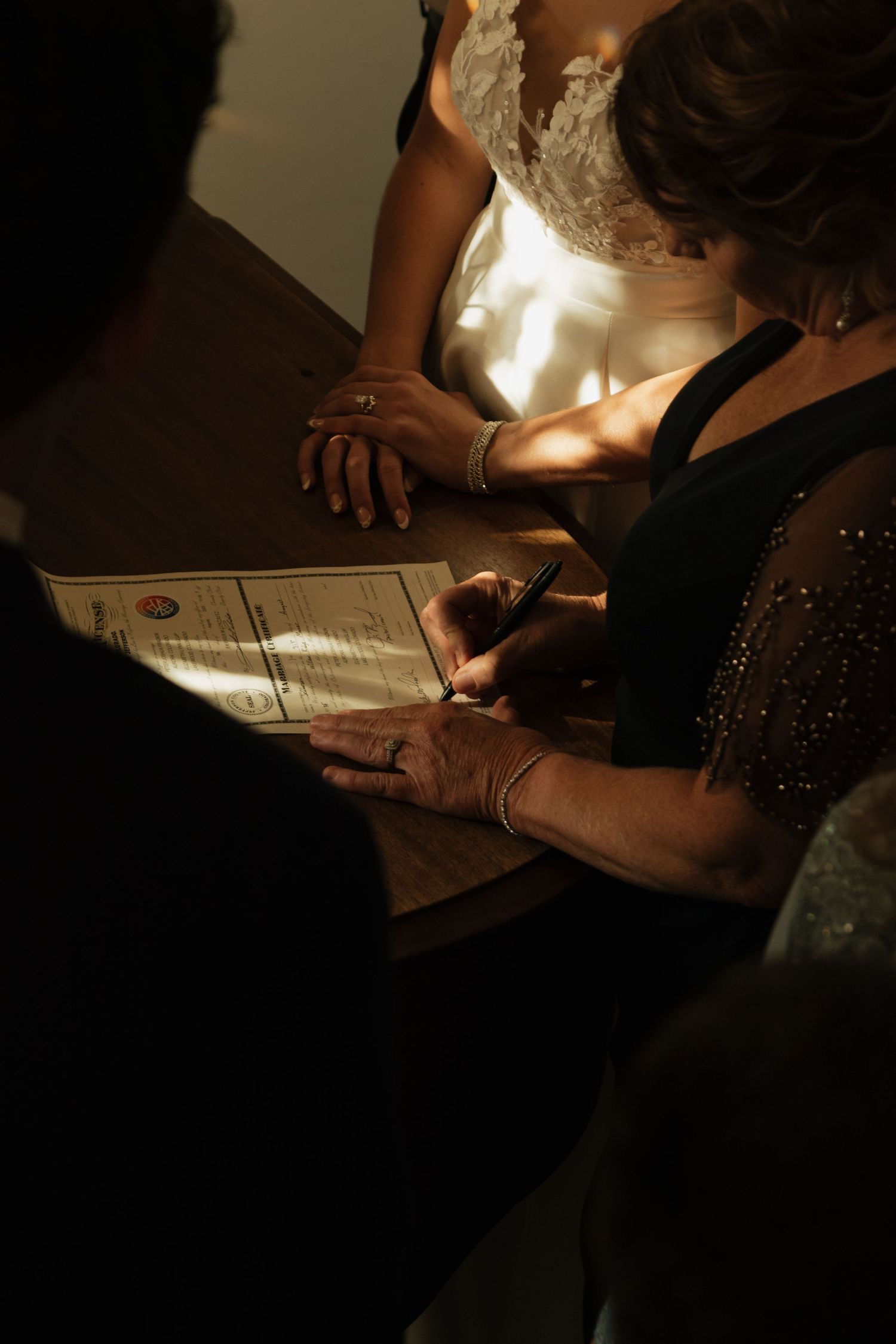 Closeup shots of hands signing wedding documents in dramatic lighting.