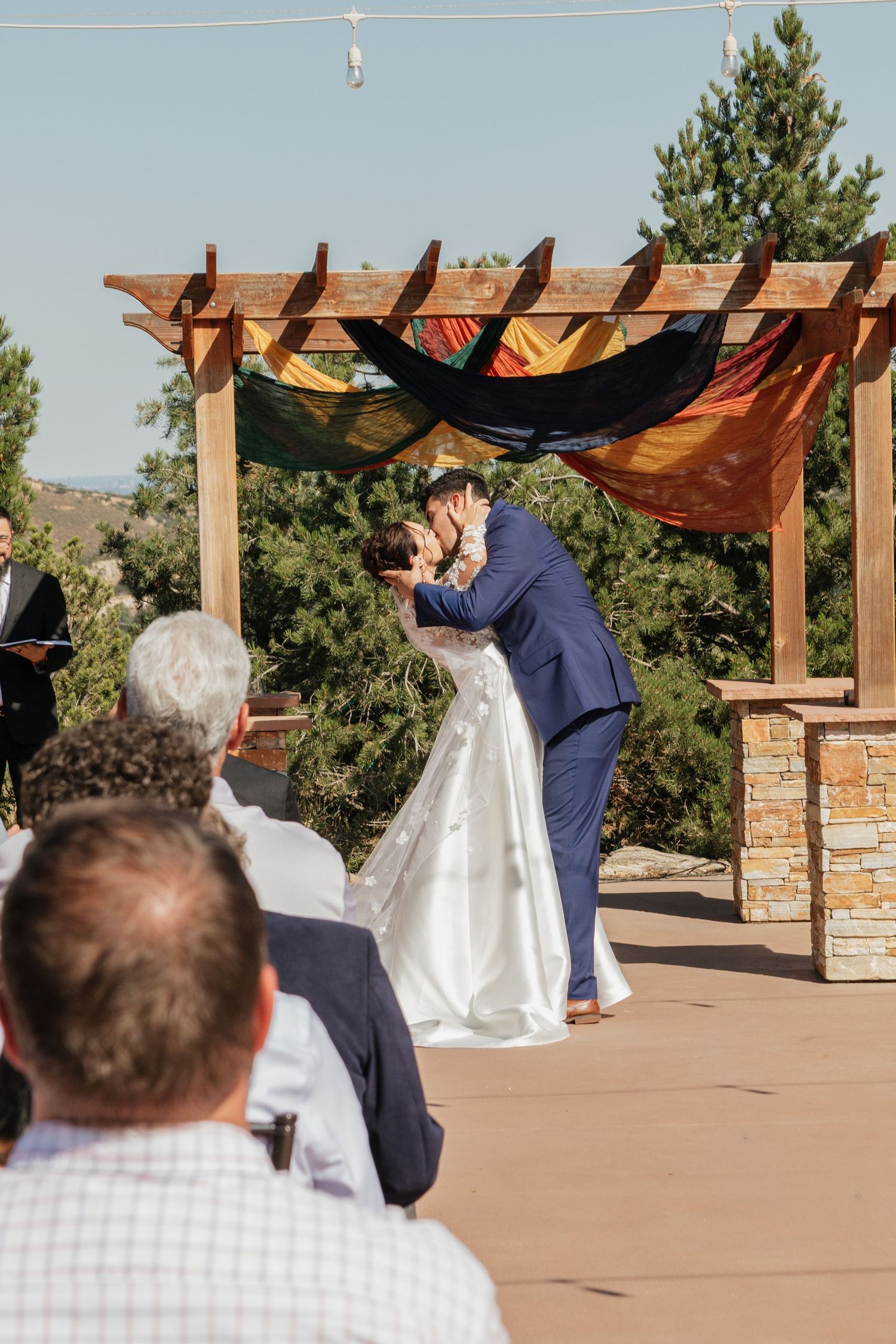 Wedding ceremony setup with wooden pergola and mountain backdrop as guests watch from their seats.