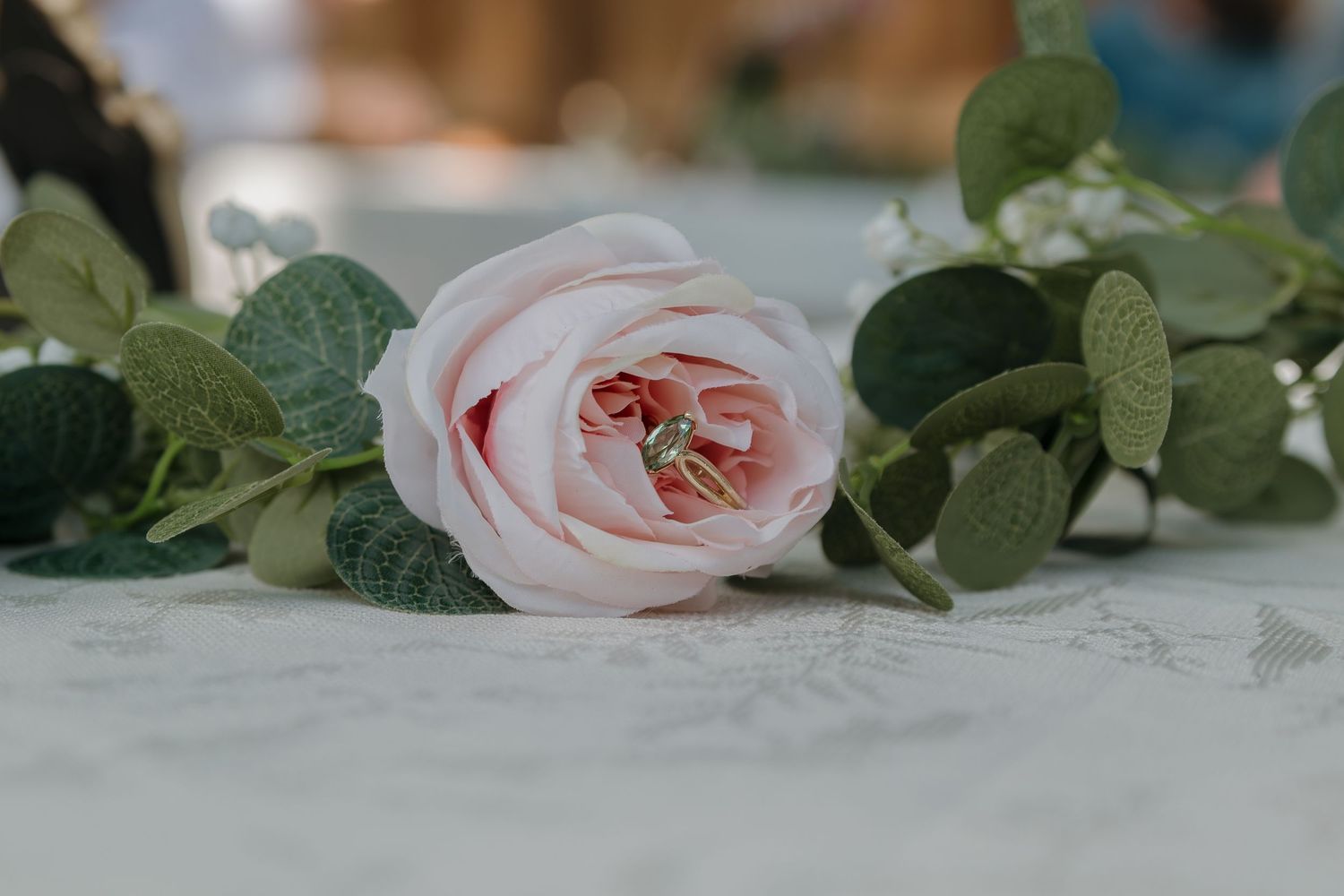 Soft pink garden roses and eucalyptus leaves arranged on a rustic white wooden surface create an elegant floral display.