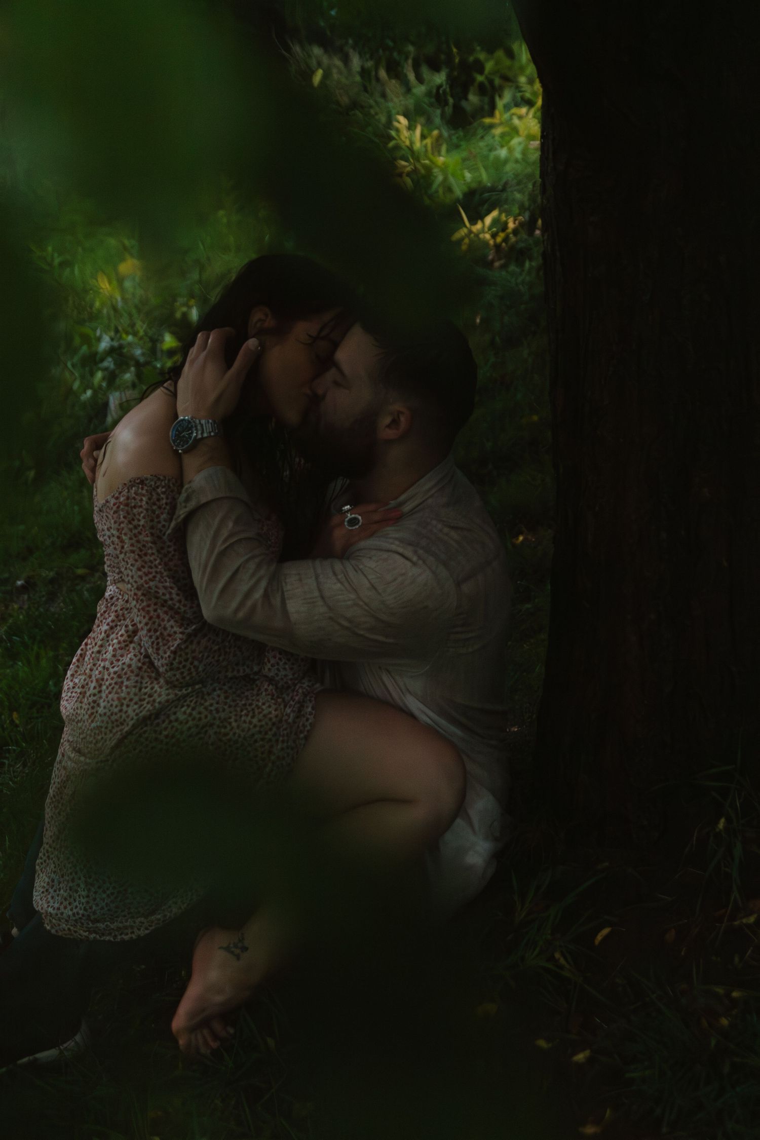 Romantic couple sharing intimate moments in a dimly lit forest setting.