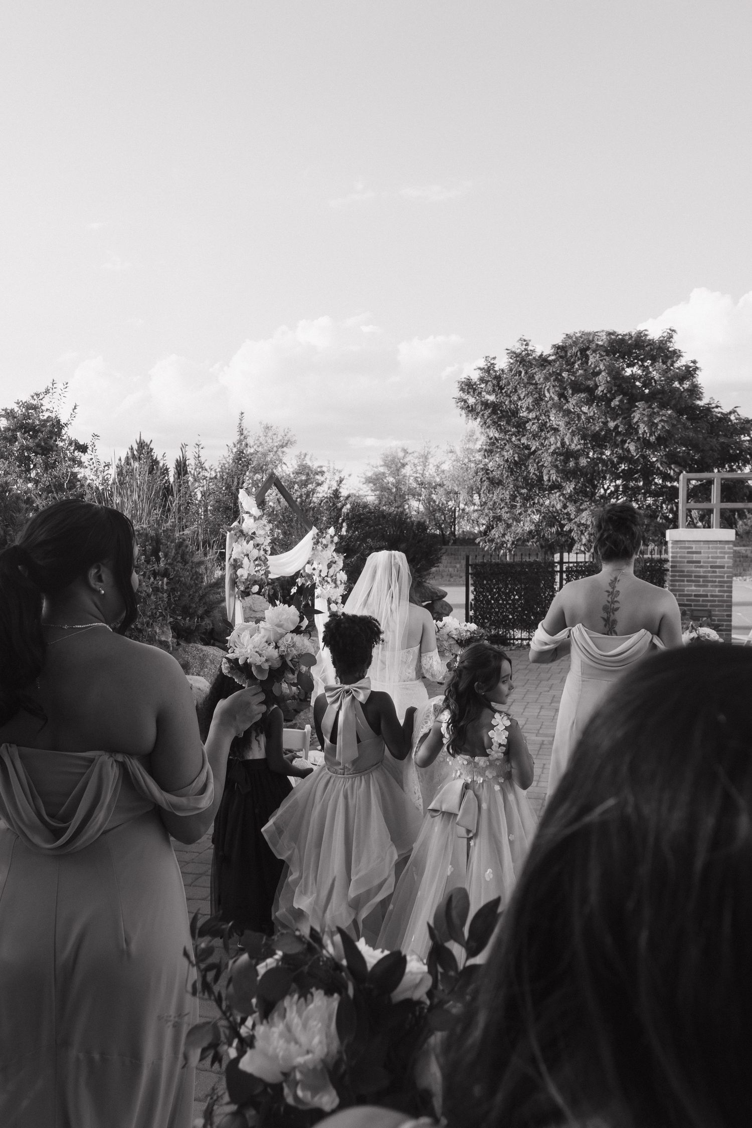 Black and white photo of bridal party processional with flower girls at outdoor wedding.