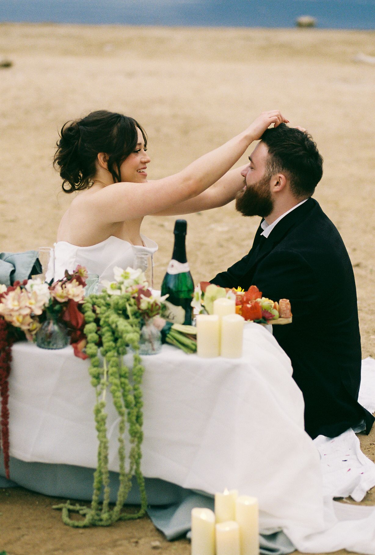 A romantic beach wedding setup with candlelit table and floral decorations at sunset.