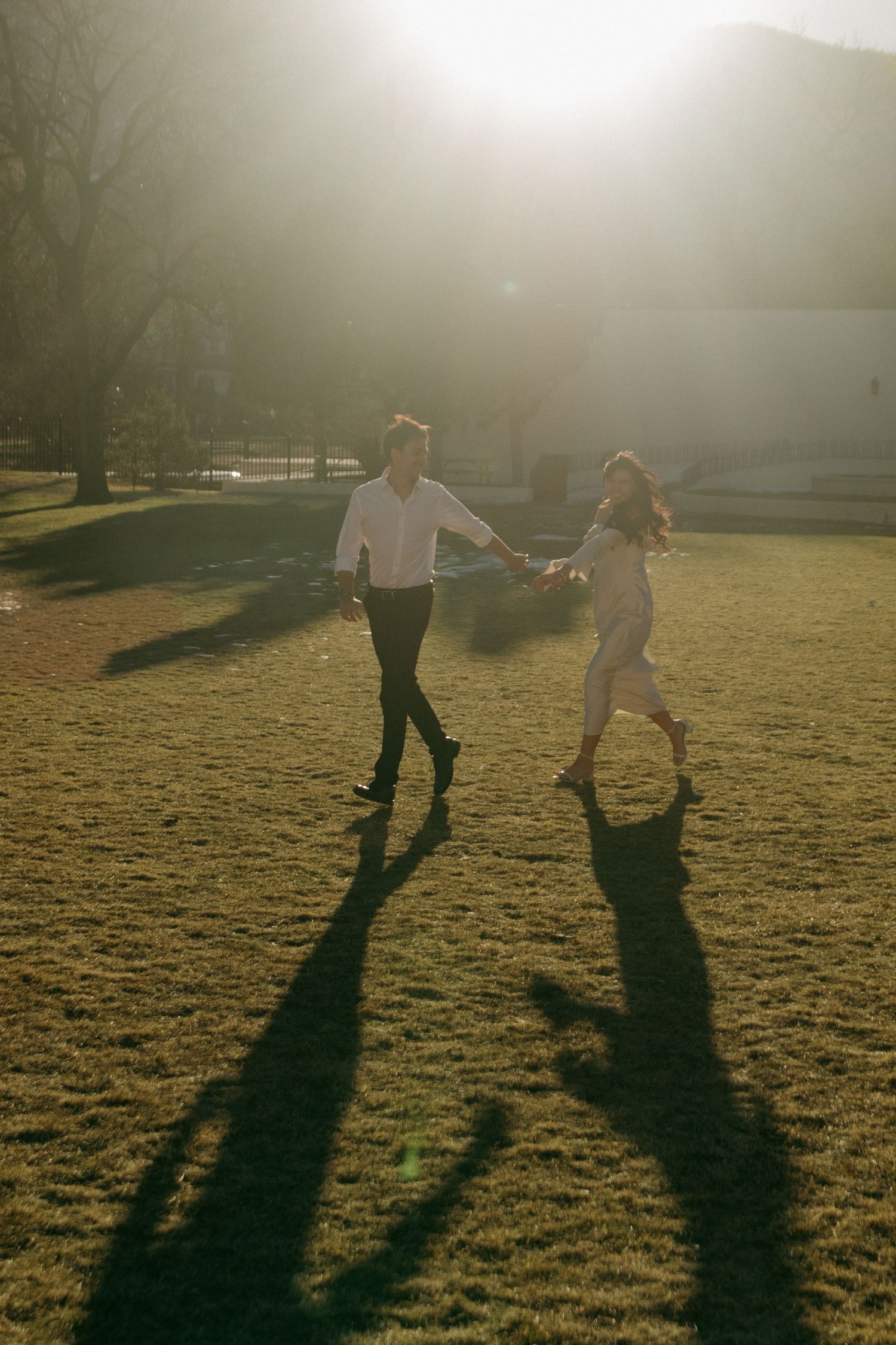 Two figures cast long shadows while playfully running through a sunlit field.