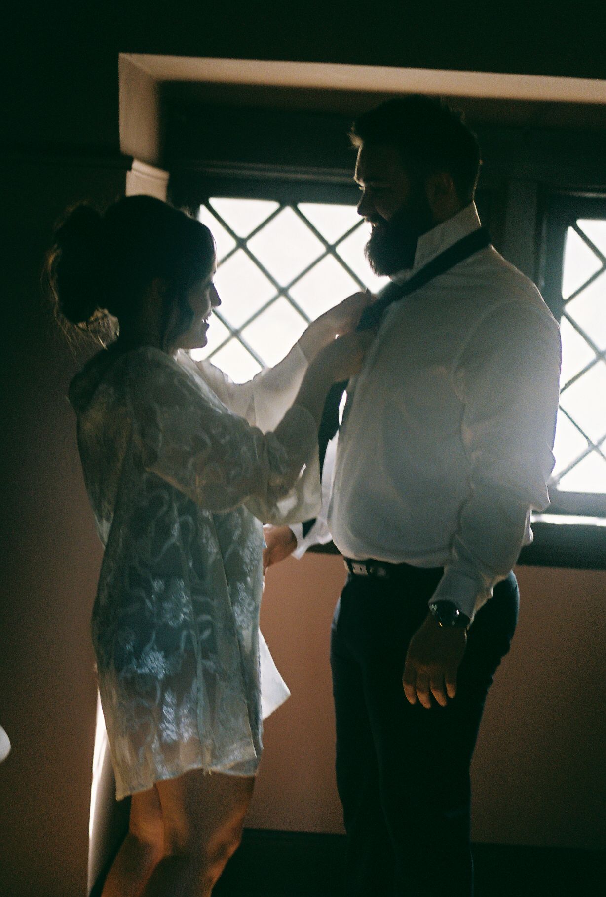 Two figures stand in silhouette against a window with diamond-patterned glass.