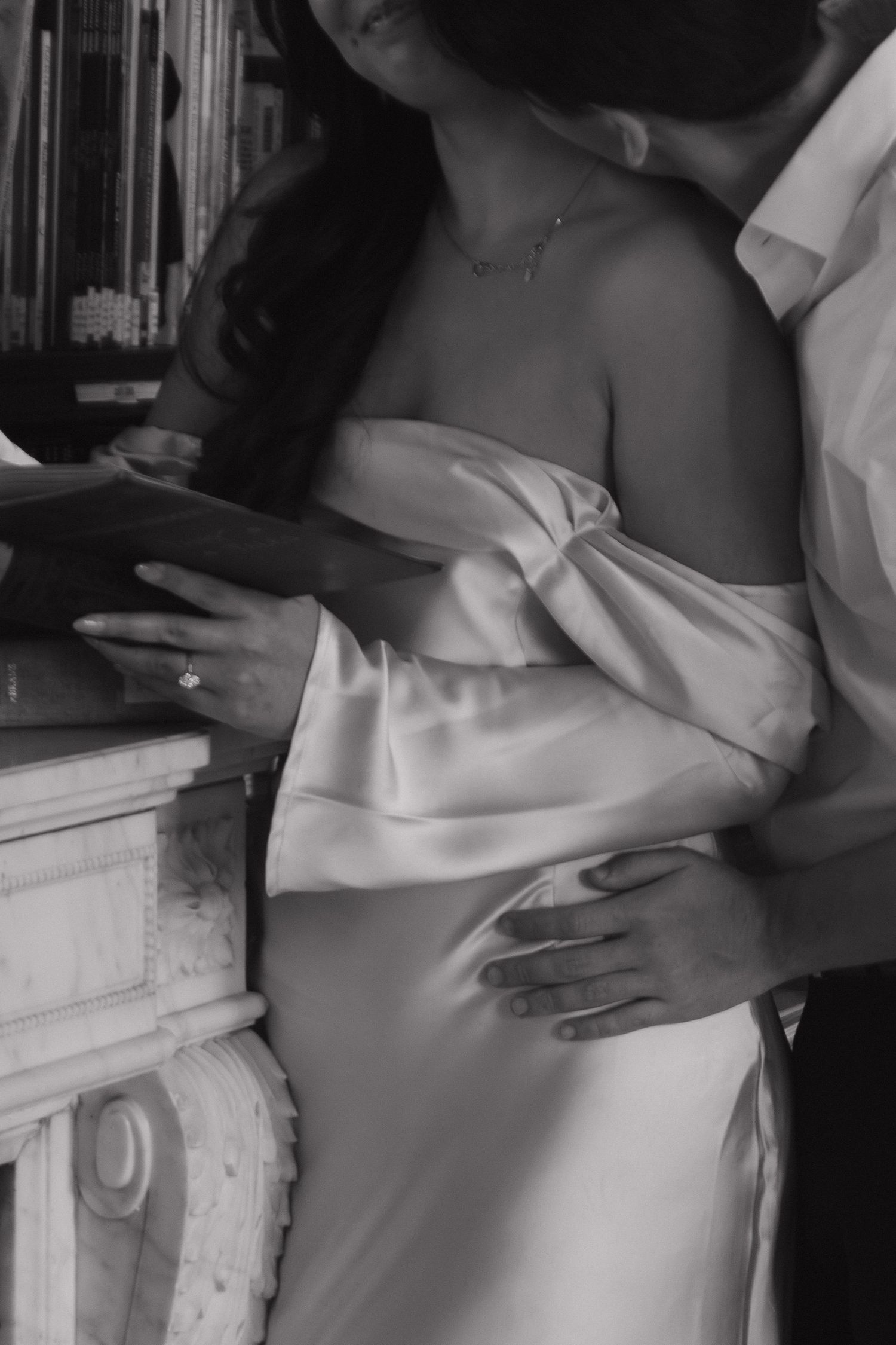 Close-up shot of a couple in white clothing embracing near a white mantelpiece.
