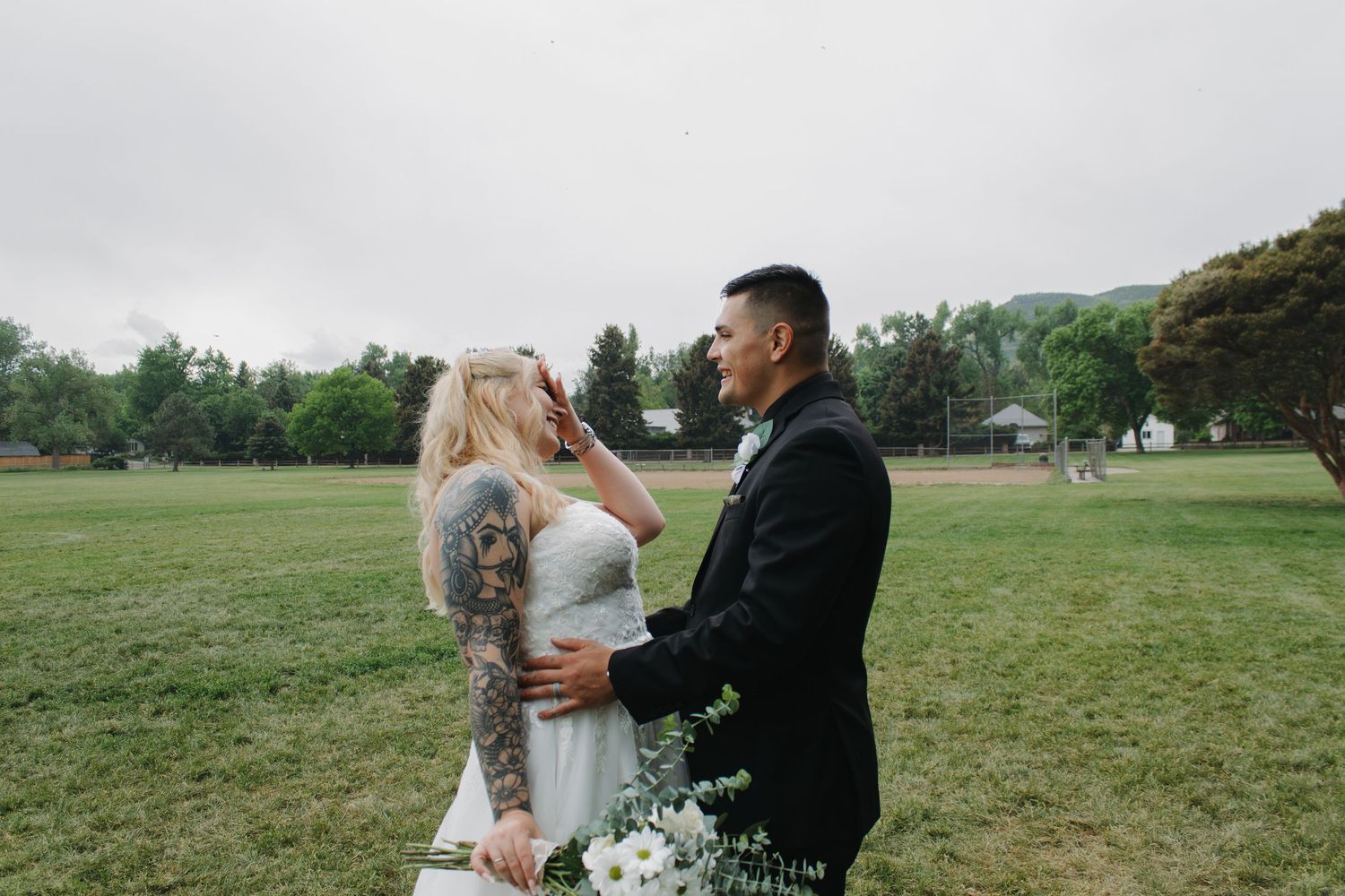 A joyful wedding moment captured in a grassy field with trees in the background.