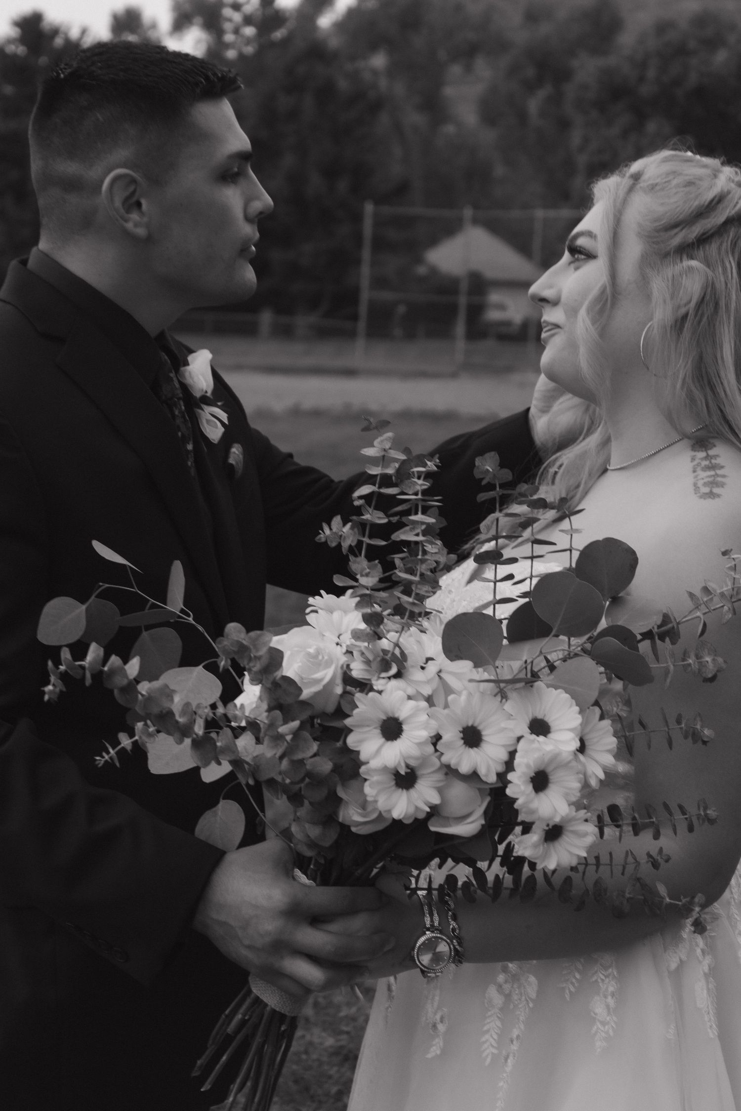 A black and white wedding photo with a couple holding a bouquet of white daisies and eucalyptus.