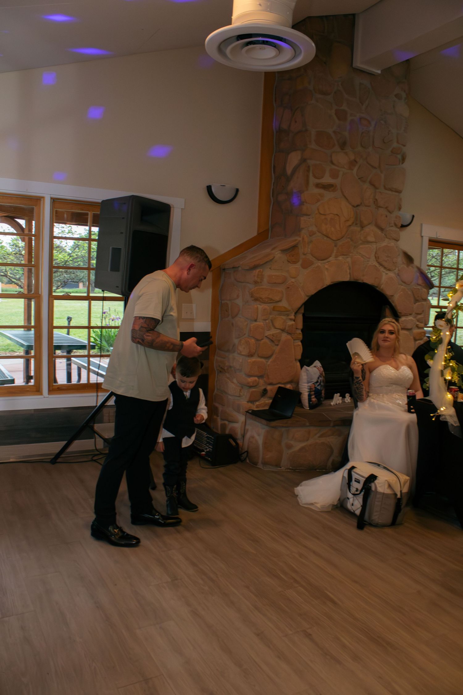 Wedding reception scene with stone fireplace, hardwood floors and colored lighting effects.
