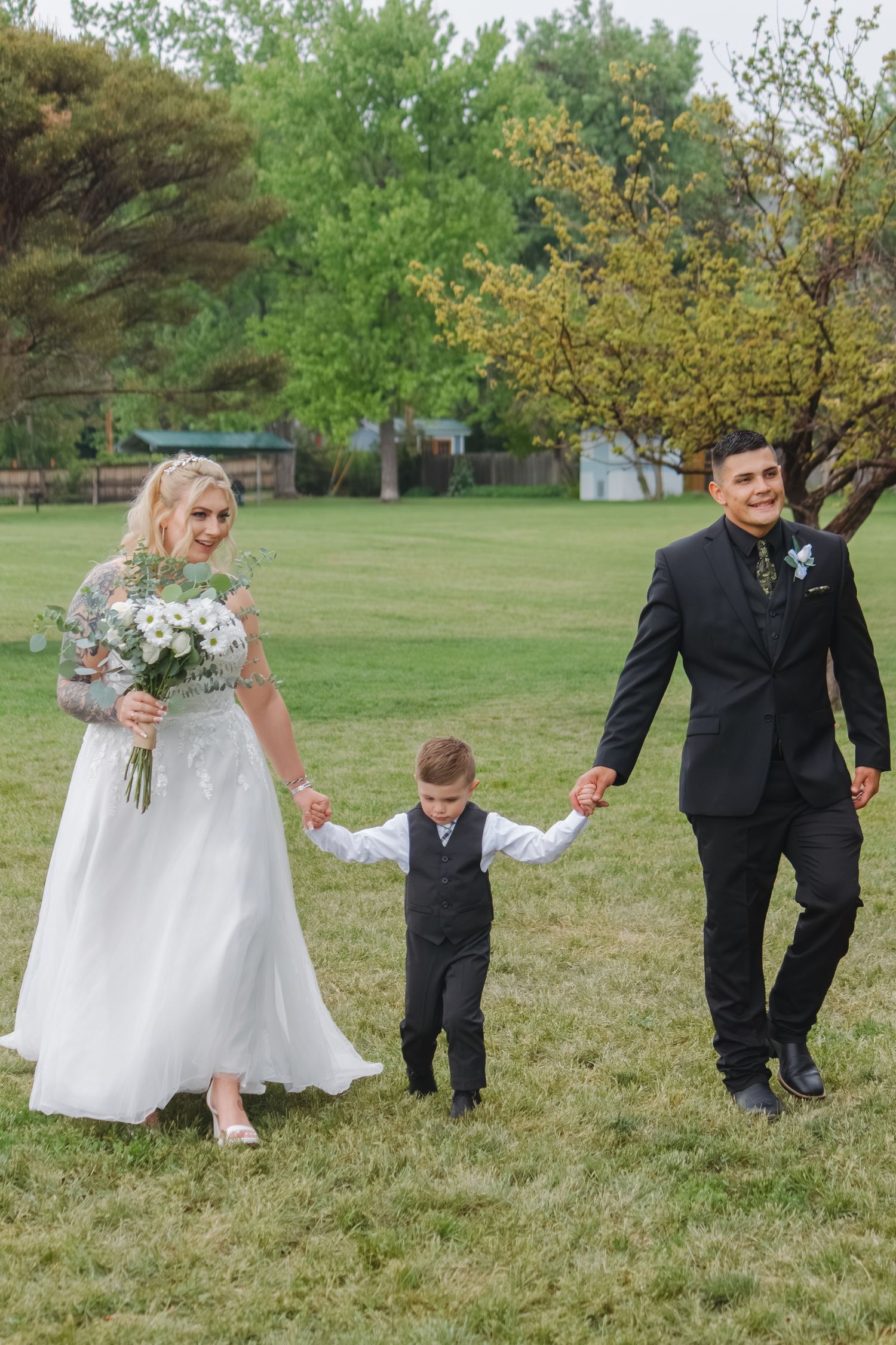 Wedding party walking hand in hand across a green lawn with spring trees in background.
