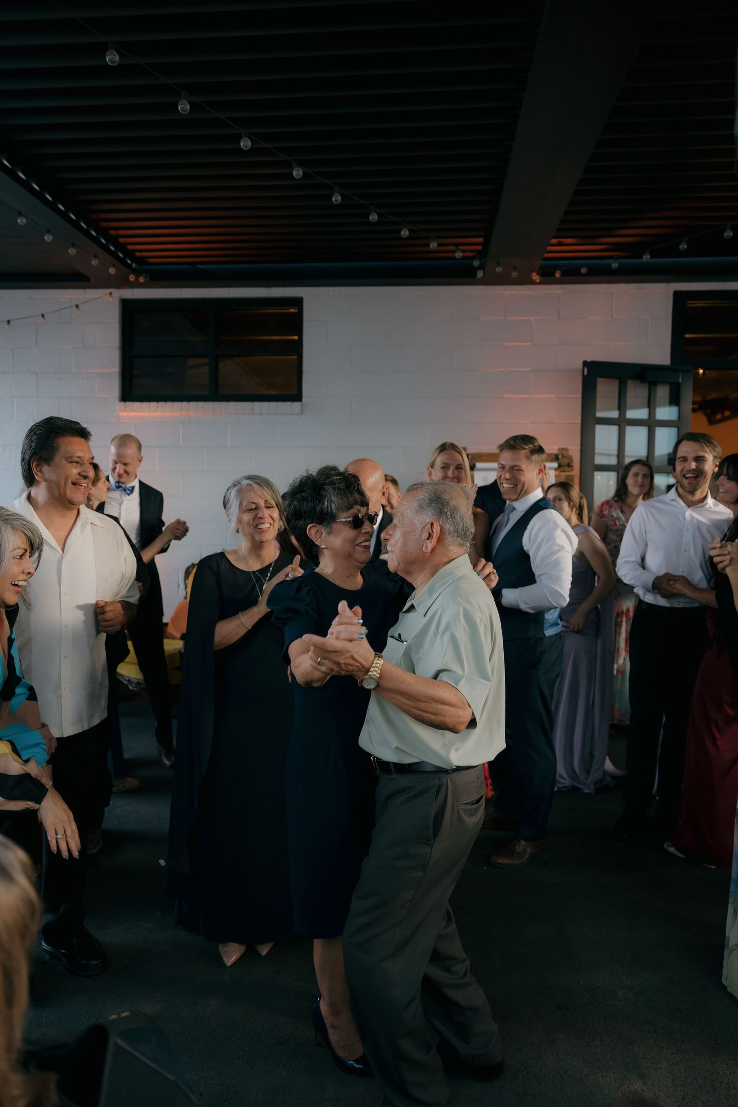Elderly couple dancing together surrounded by guests at a wedding reception.