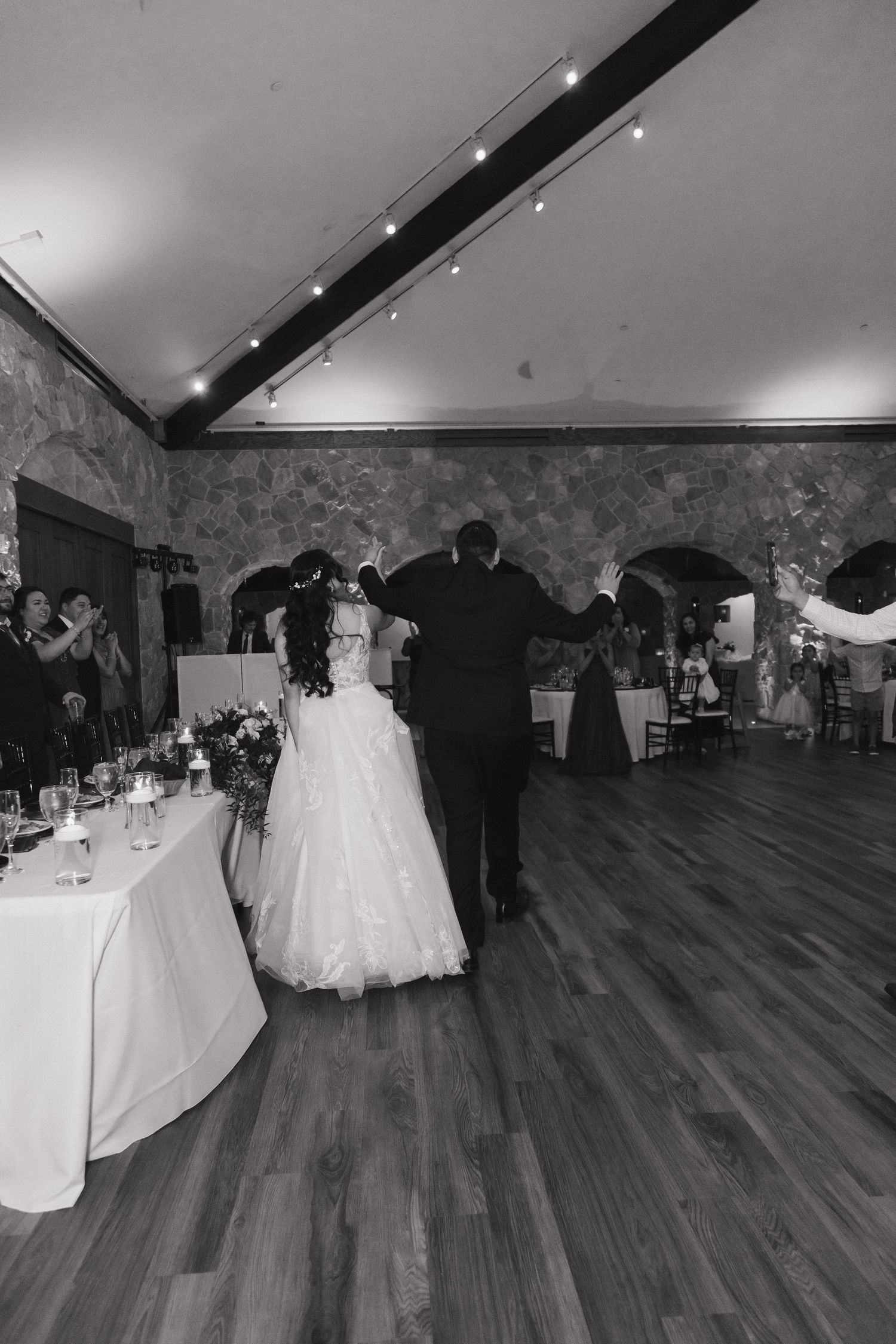 Black and white photo of bride and groom sharing their first dance in an elegant stone ballroom.