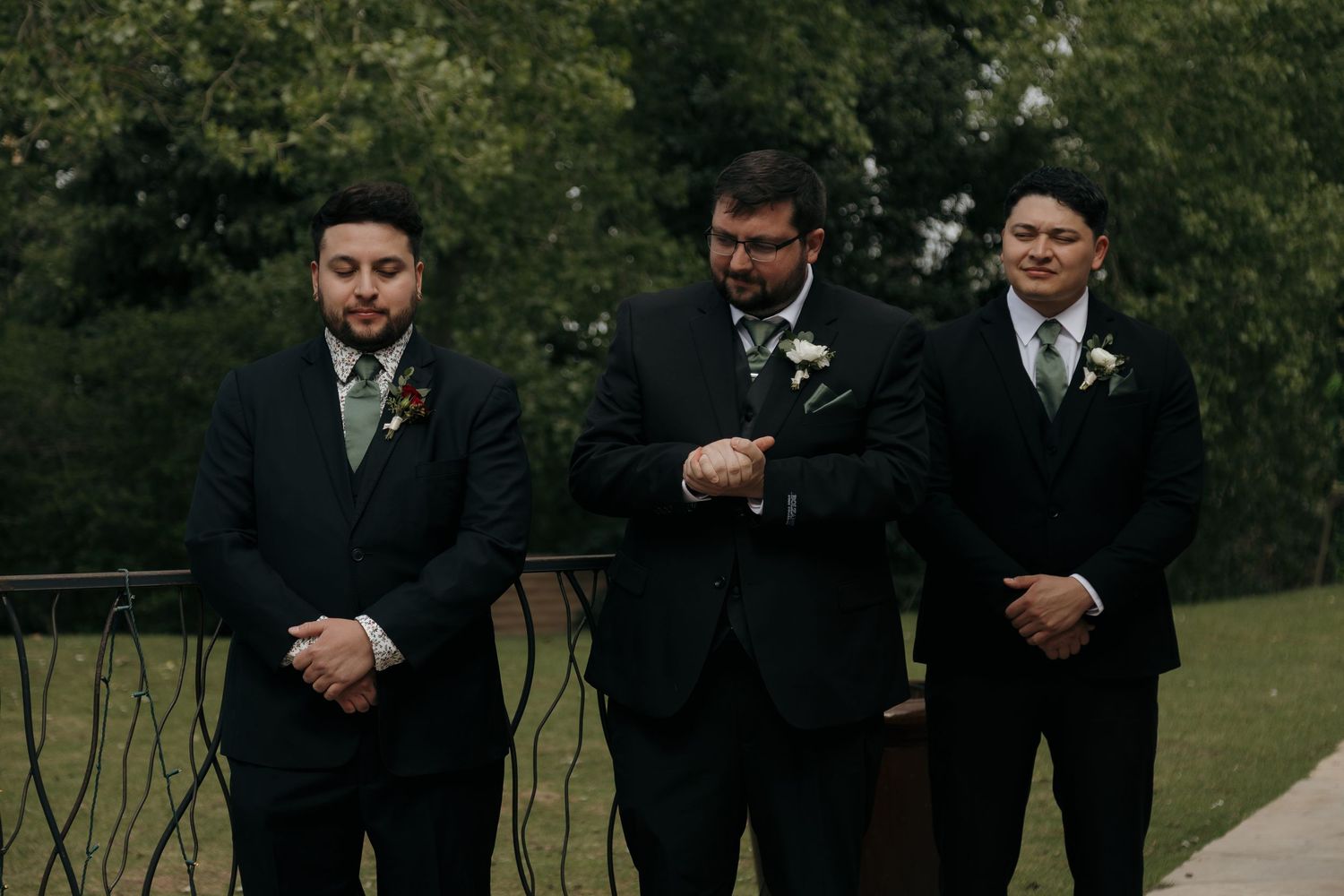 Groom checks his watch while flanked by two groomsmen in dark suits before the wedding ceremony.