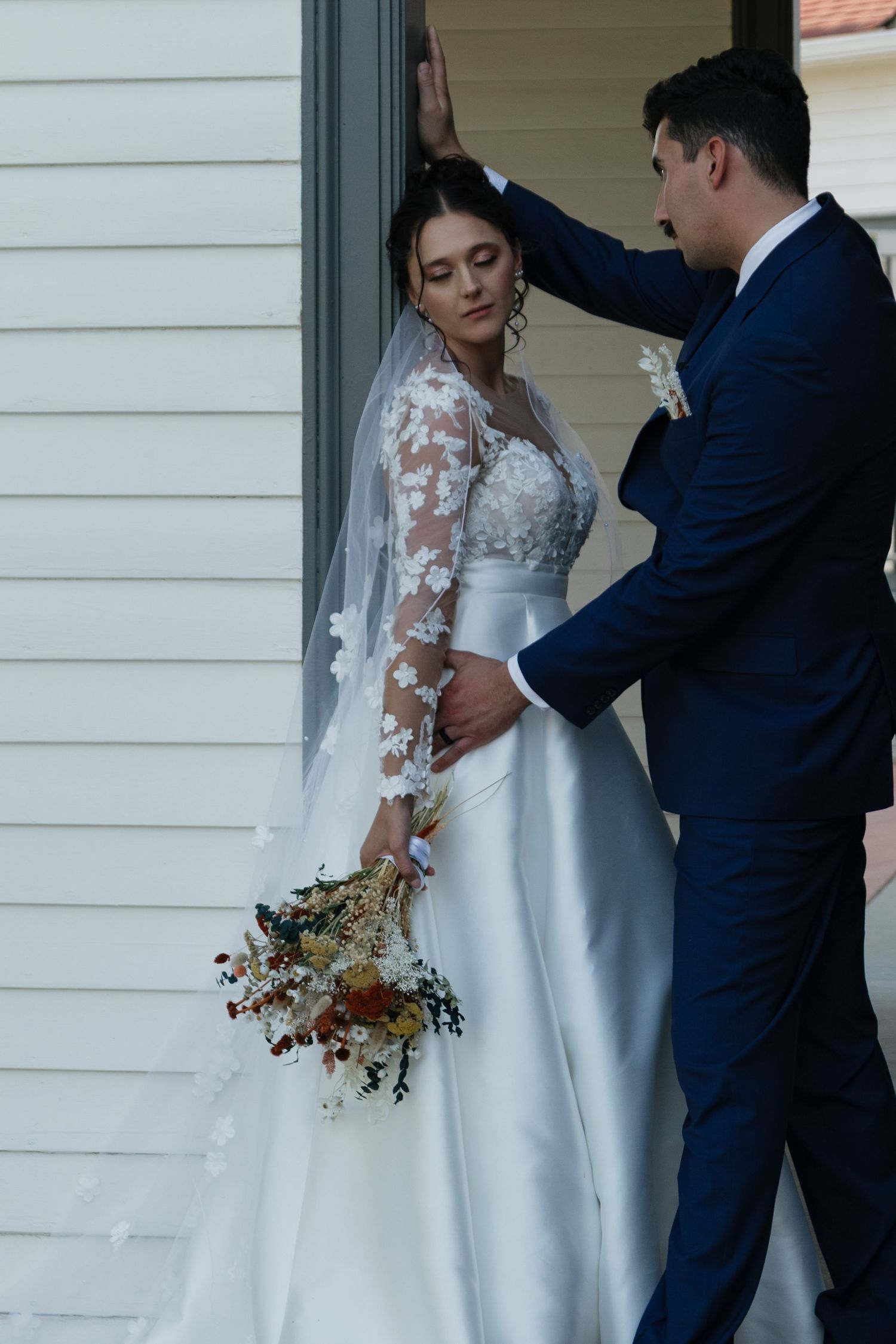 Intimate wedding moment captured on a white building's porch with autumn floral bouquet.