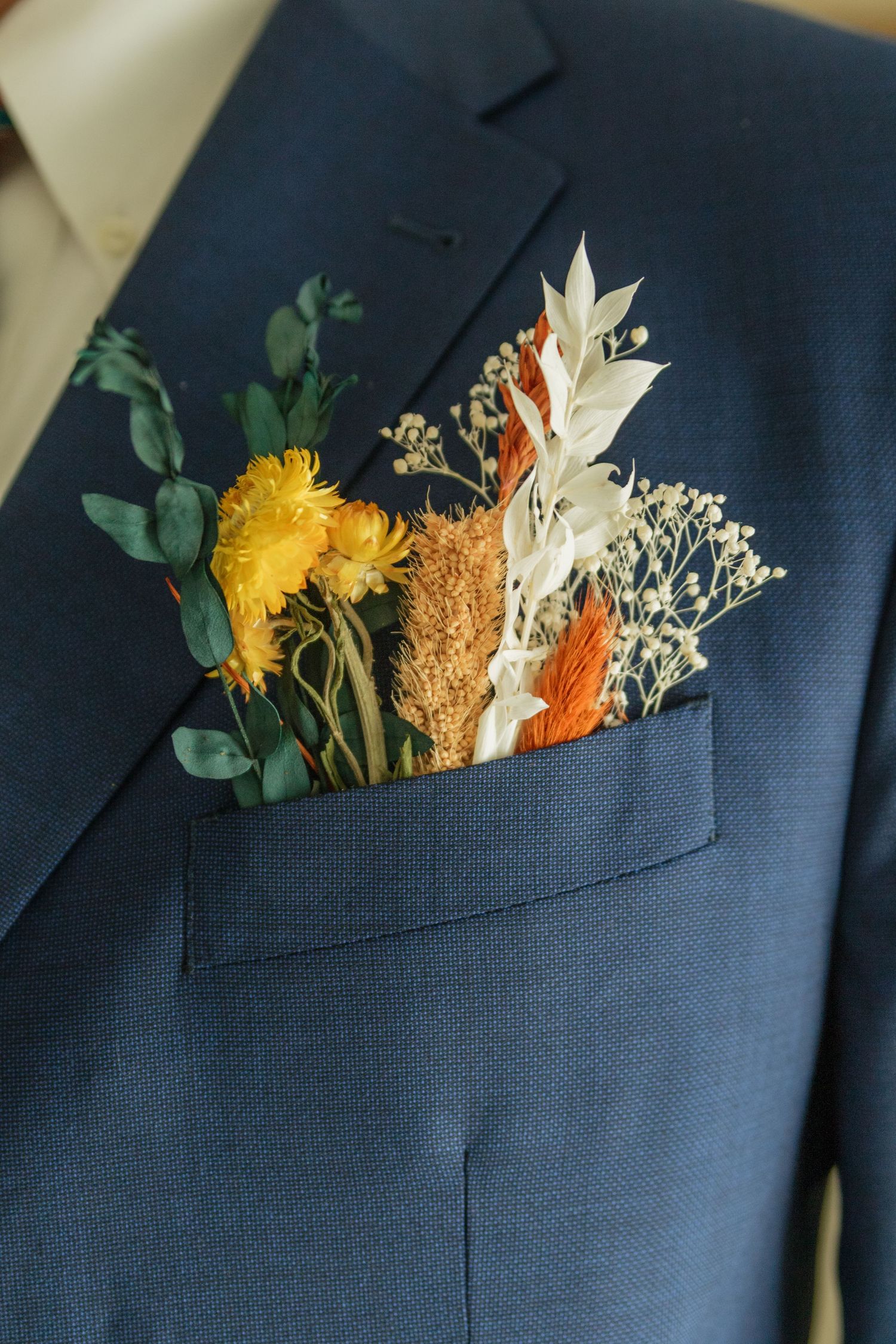 Colorful floral boutonniere with yellow and orange flowers tucked into navy suit pocket.