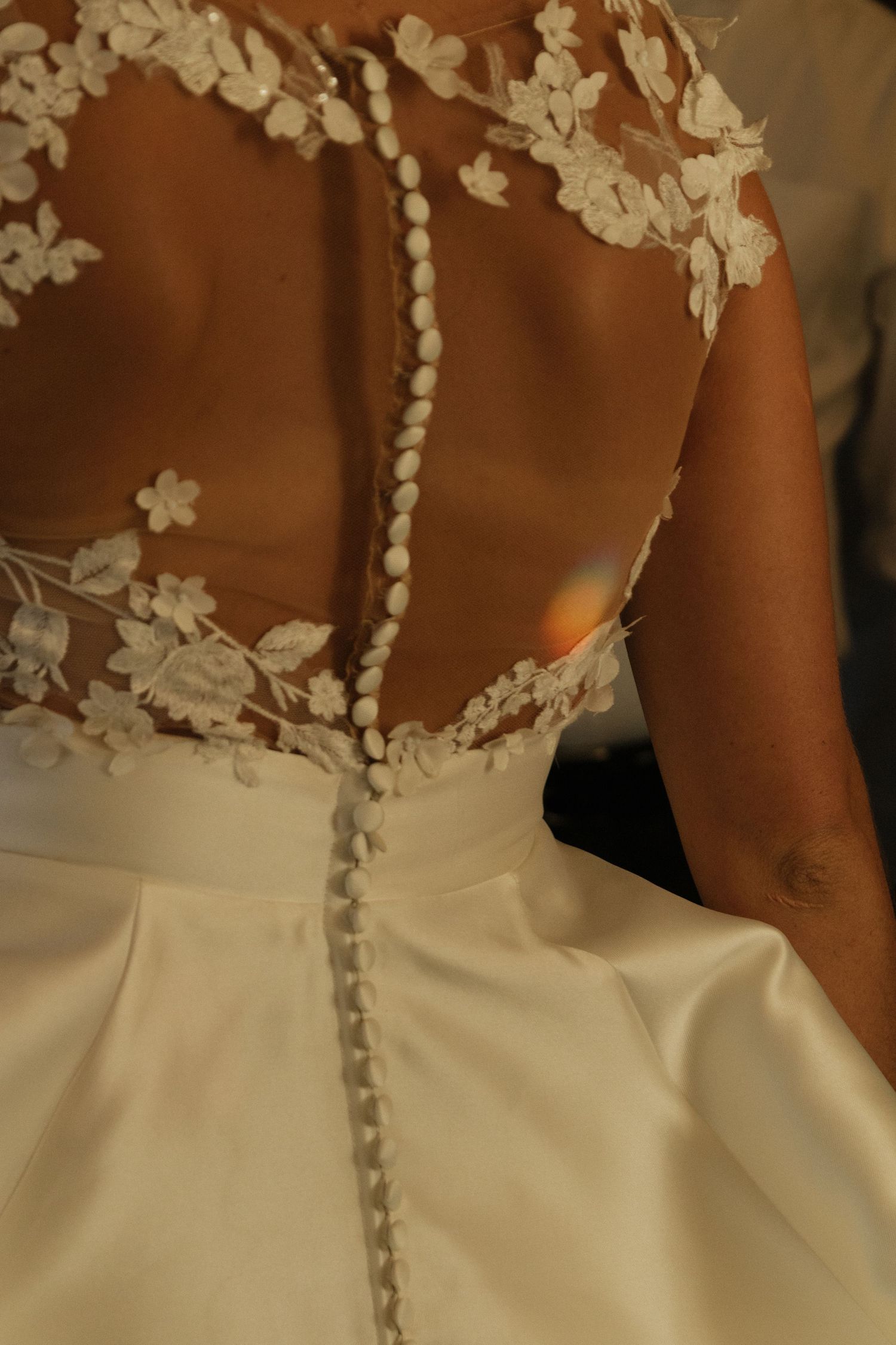 Close-up detail of a wedding dress back with delicate floral lace appliques and button closures.