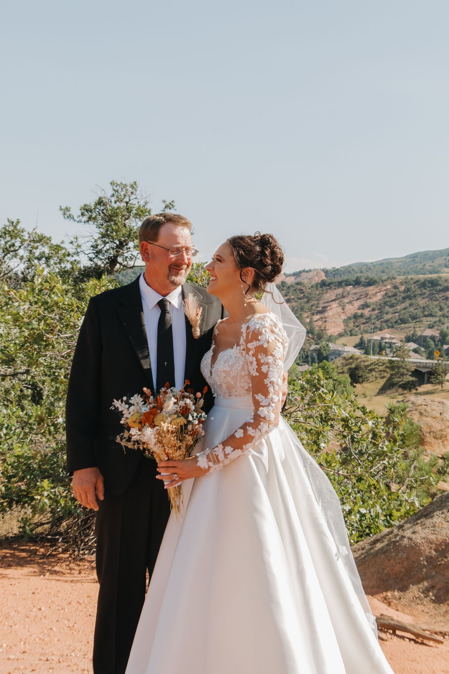 Couple in wedding attire embrace on a scenic mountain overlook during sunset.