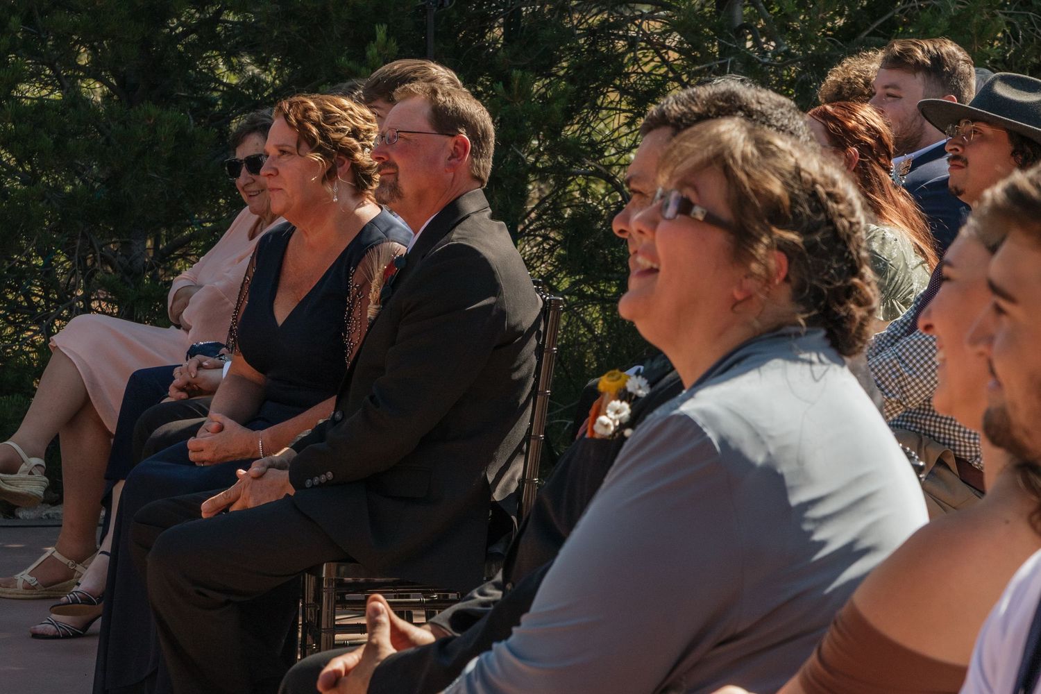Guests watching an outdoor wedding ceremony while seated in rows with natural foliage behind them.