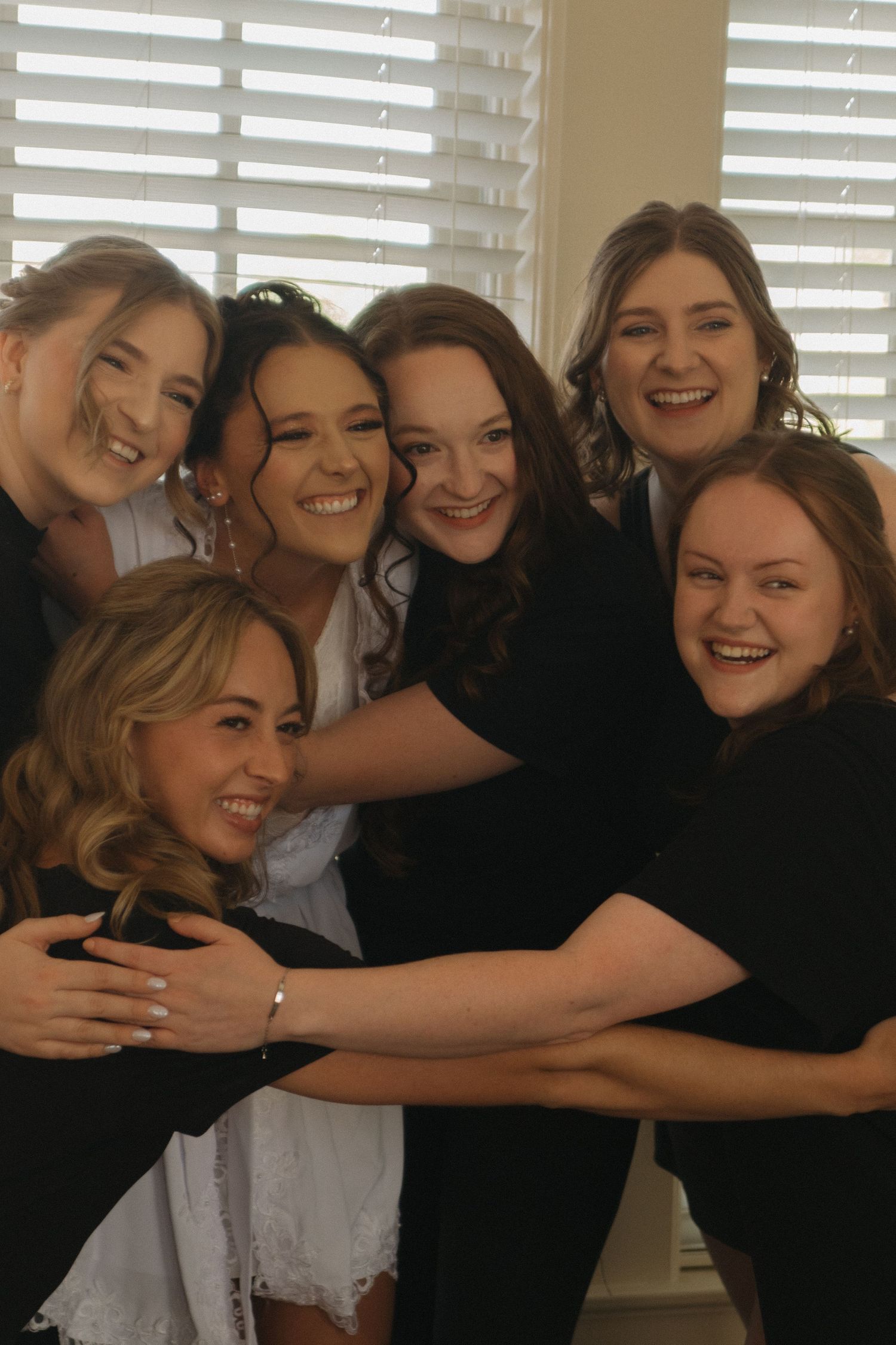 A group of friends hugging and laughing together while wearing black and white outfits.
