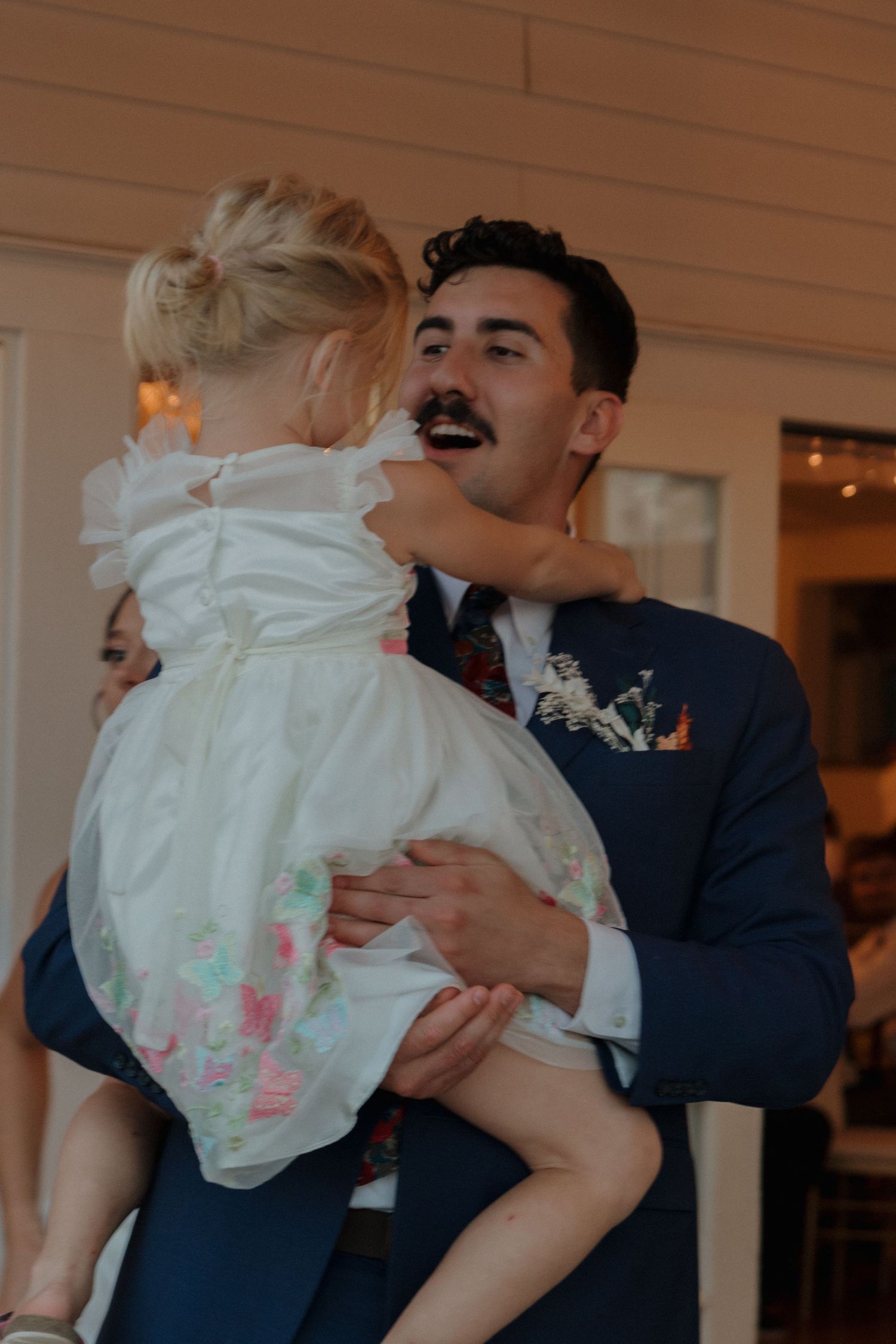 Tender moment shared between a man in navy suit holding a small child in white dress.