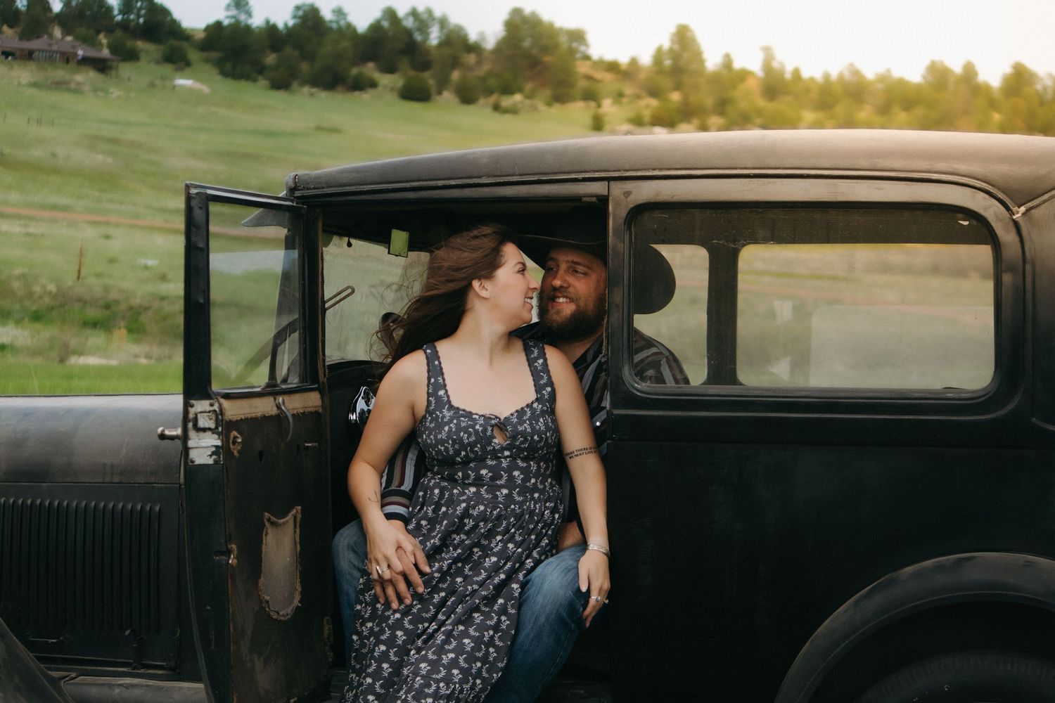 Romantic vintage scene with couple sitting in classic black car at sunset.