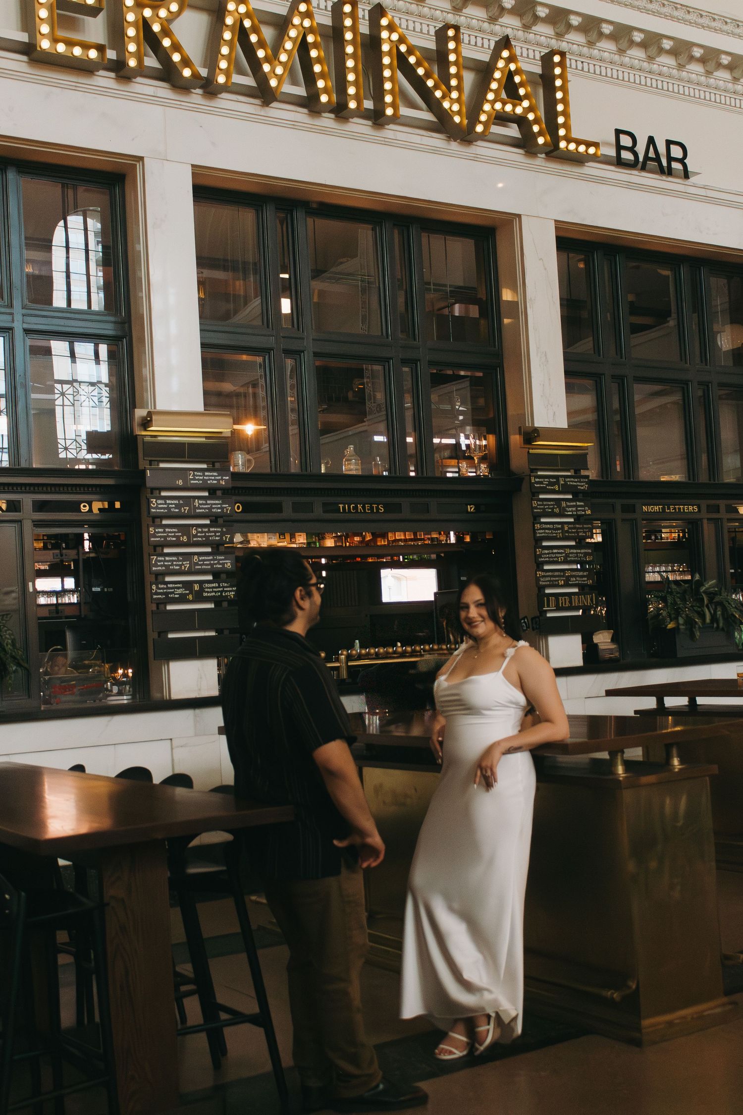 Couple conversing at Terminal Bar's entrance beneath illuminated vintage signage.