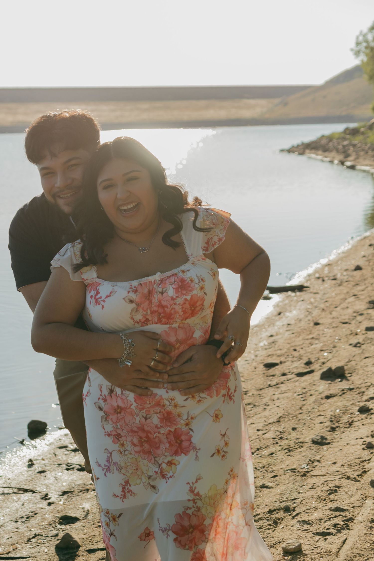 A happy couple embraces by the water's edge during golden hour.