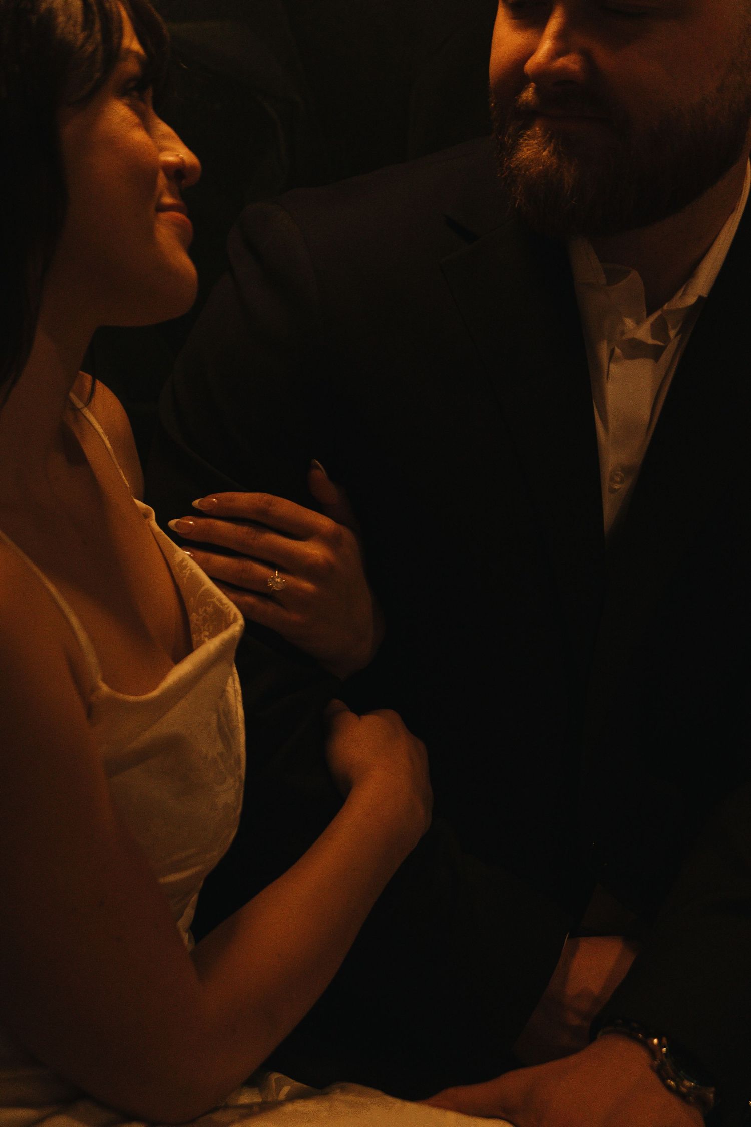 A romantic couple shares a tender moment in warm amber lighting with formal evening attire.