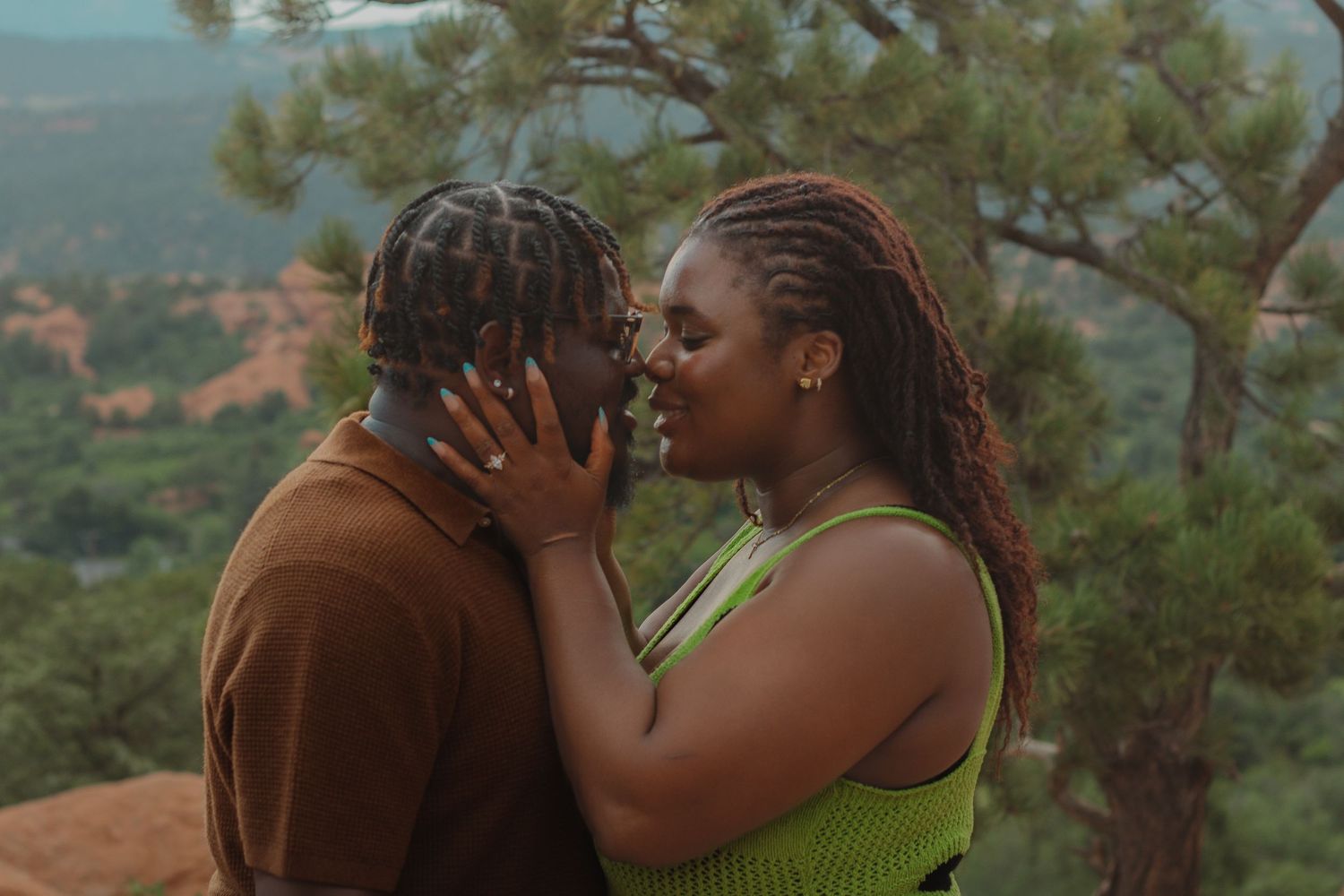 A loving couple embraces against a scenic mountain landscape backdrop.