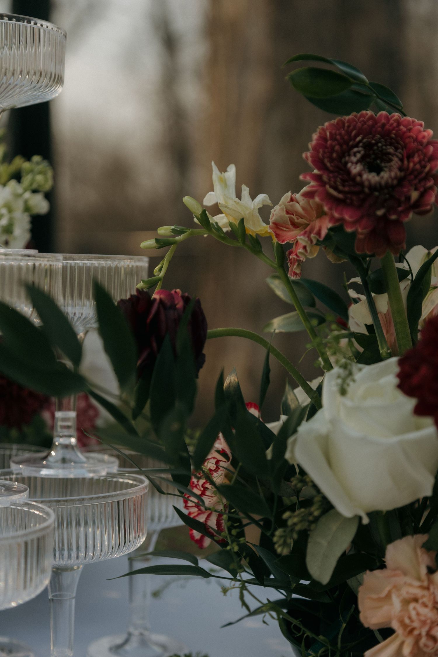 Close-up of elegant wedding floral arrangement with burgundy dahlias, white roses, and crystal glassware.