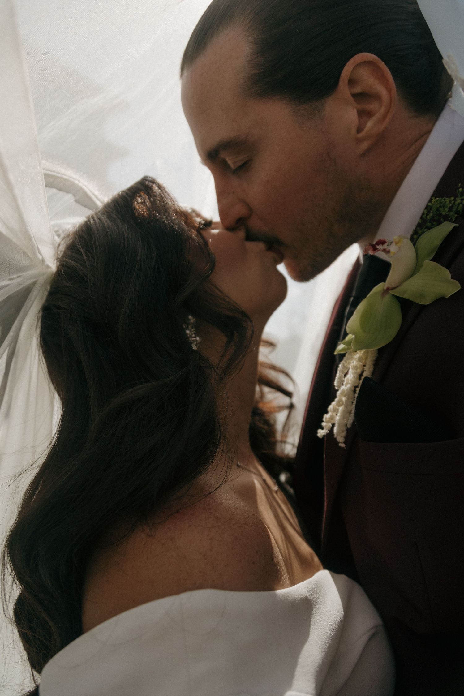 Bride and groom share a romantic first kiss under a wedding veil at their ceremony.