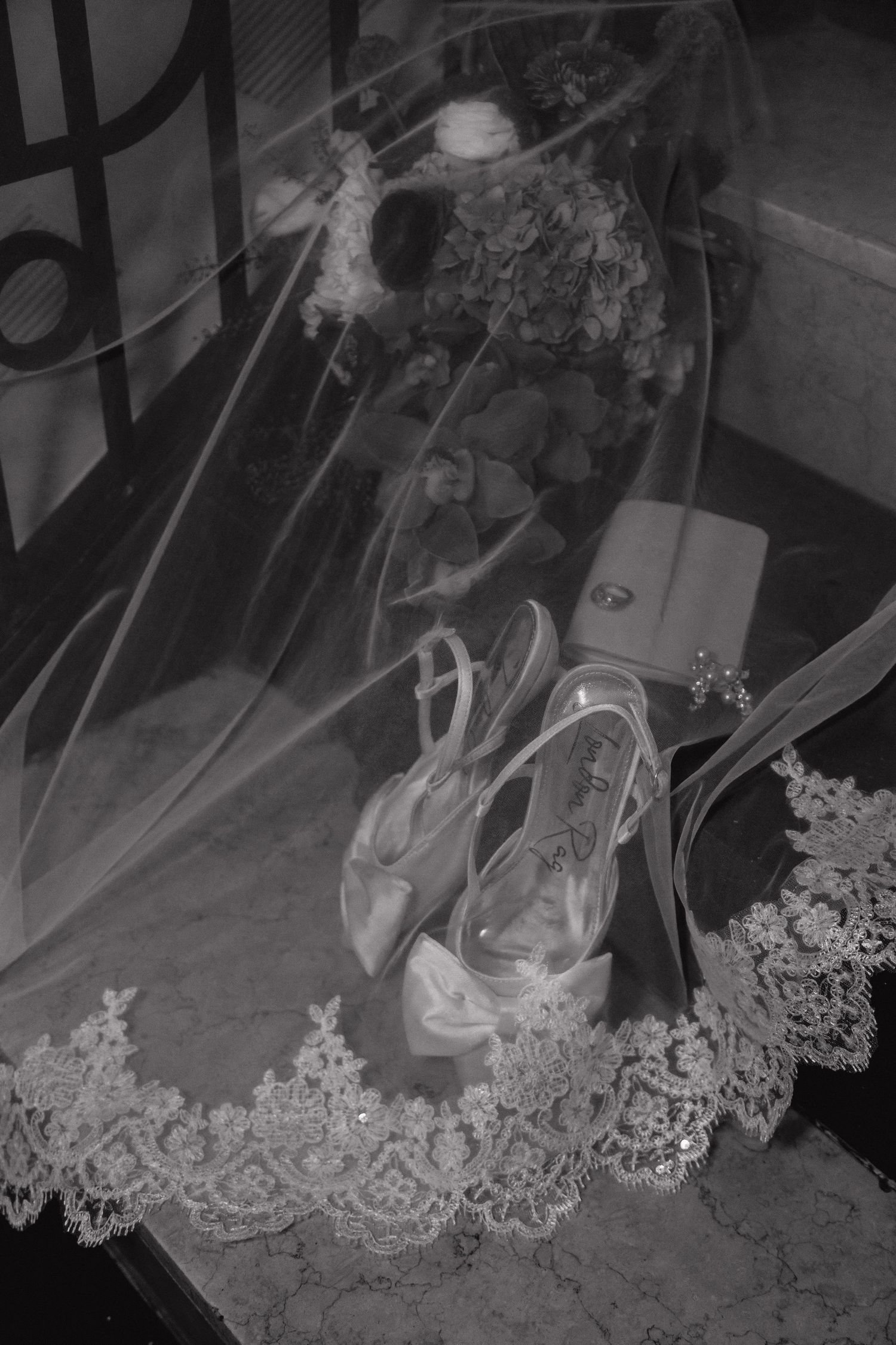 Bridal heels, veil with lace trim, bouquet and accessories arranged on marble floor.