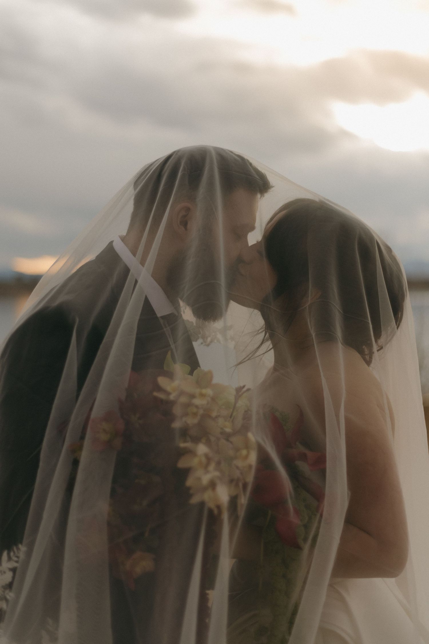 A romantic sunset wedding photo with the couple sharing a kiss under their veils.