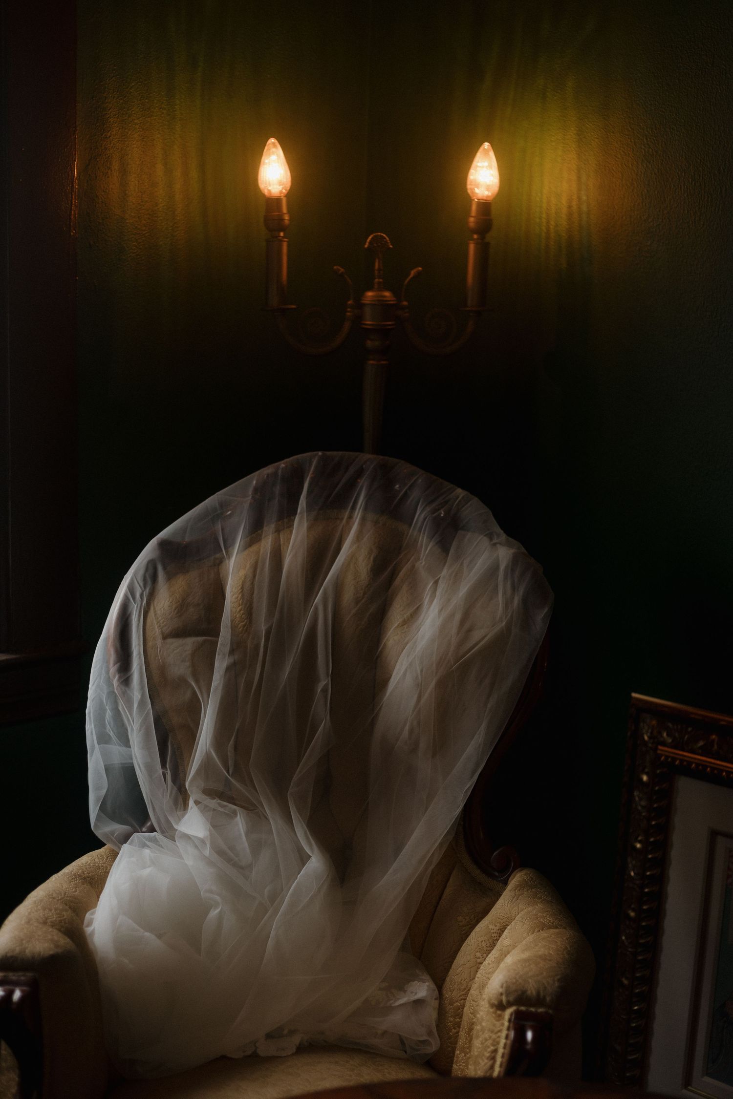 A dramatic scene with two glowing candles above a chair draped in ethereal white tulle fabric.
