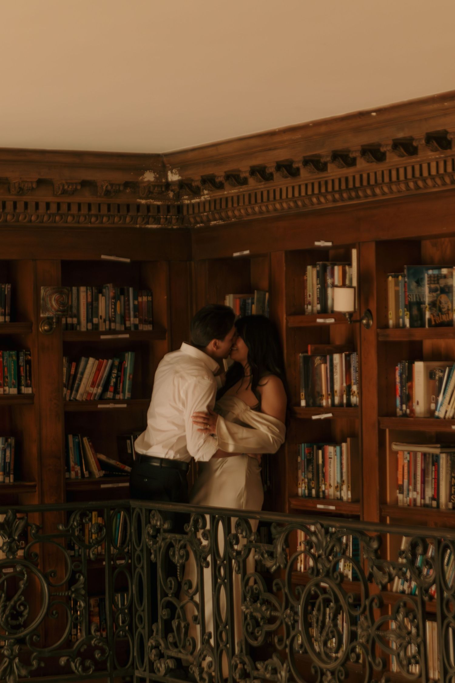 A couple shares a romantic moment in a wood-paneled library with ornate details.