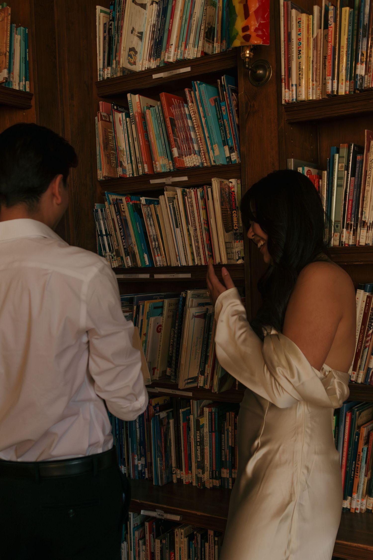 People browsing books on wooden library shelves in a dimly lit room.