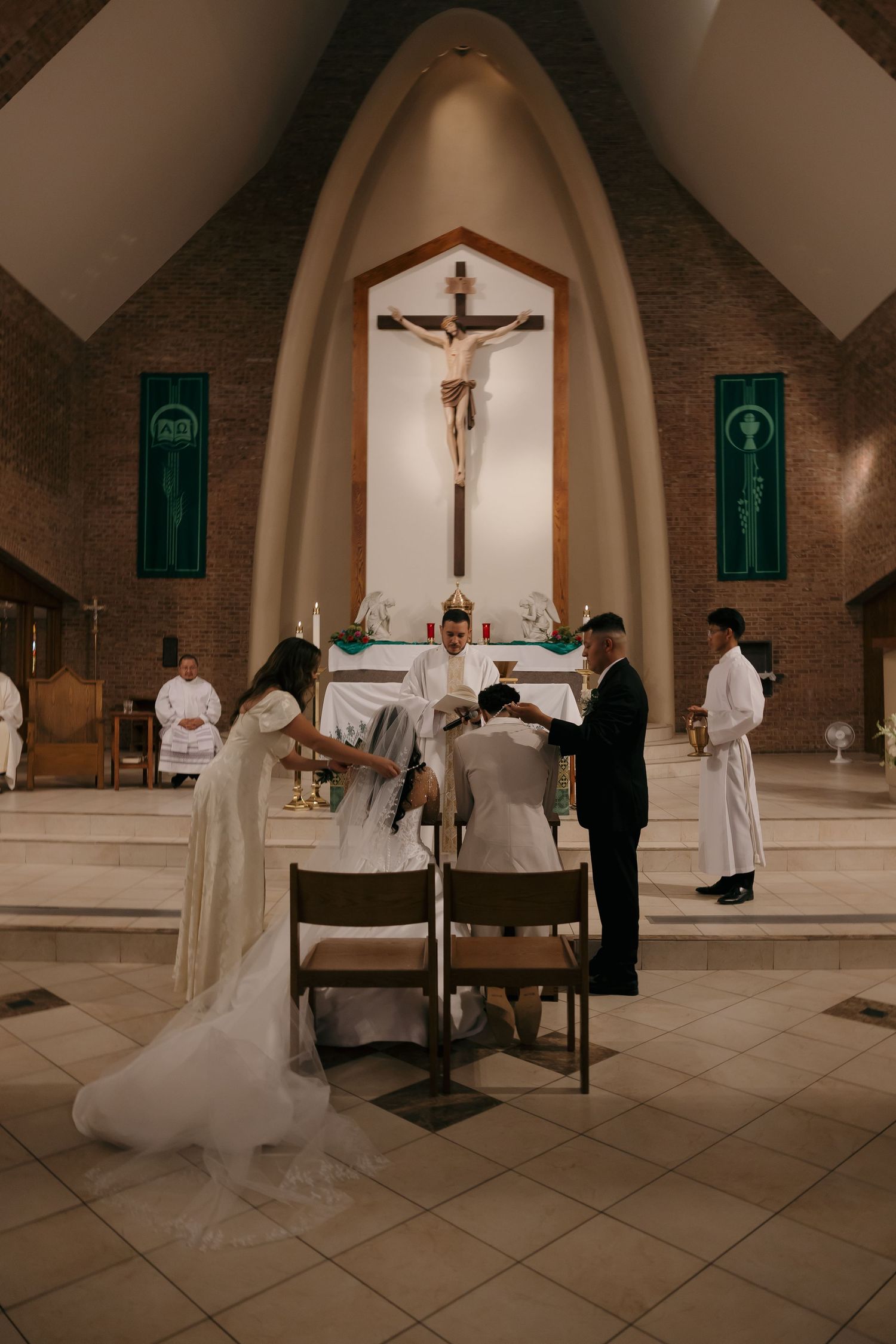 Catholic wedding ceremony at the altar with bride and groom kneeling before a crucifix.