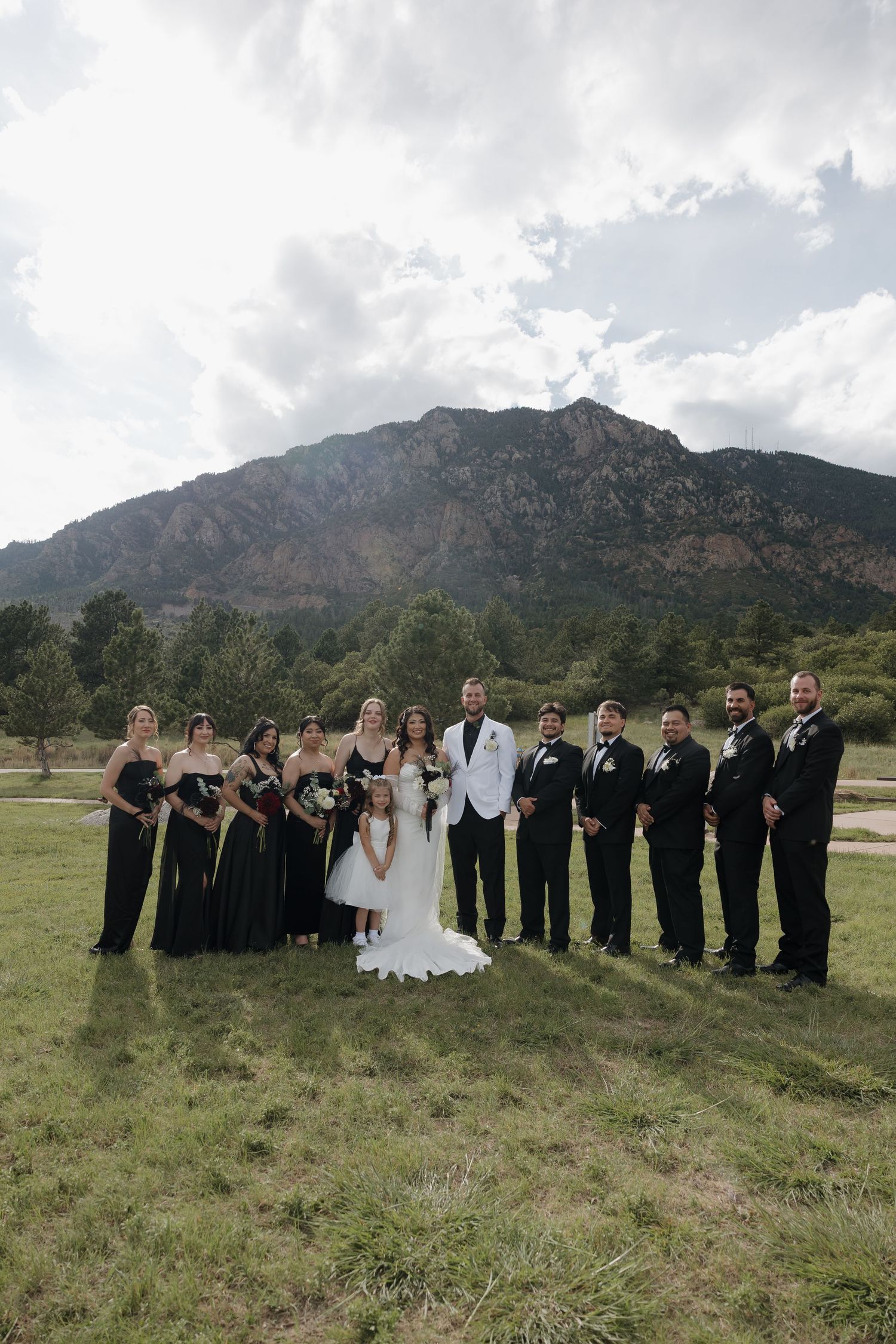 Wedding party poses in front of a stunning Rocky Mountain backdrop on a cloudy day.