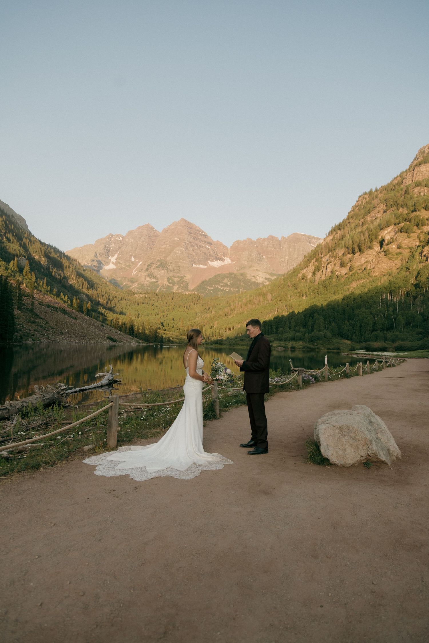 Bride and groom exchange vows at Maroon Bells lake in Colorado, surrounded by stunning mountain scenery at sunset.