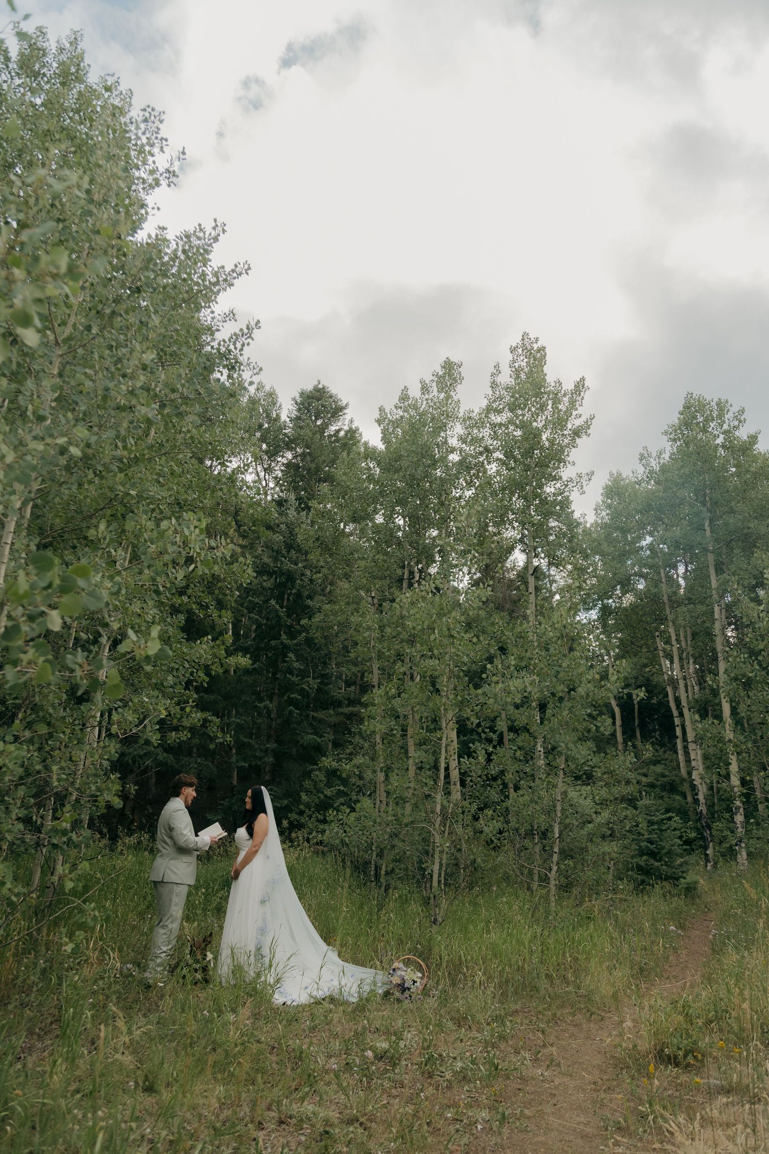 Couple shares a romantic moment in a verdant forest clearing on their outdoor wedding day.
