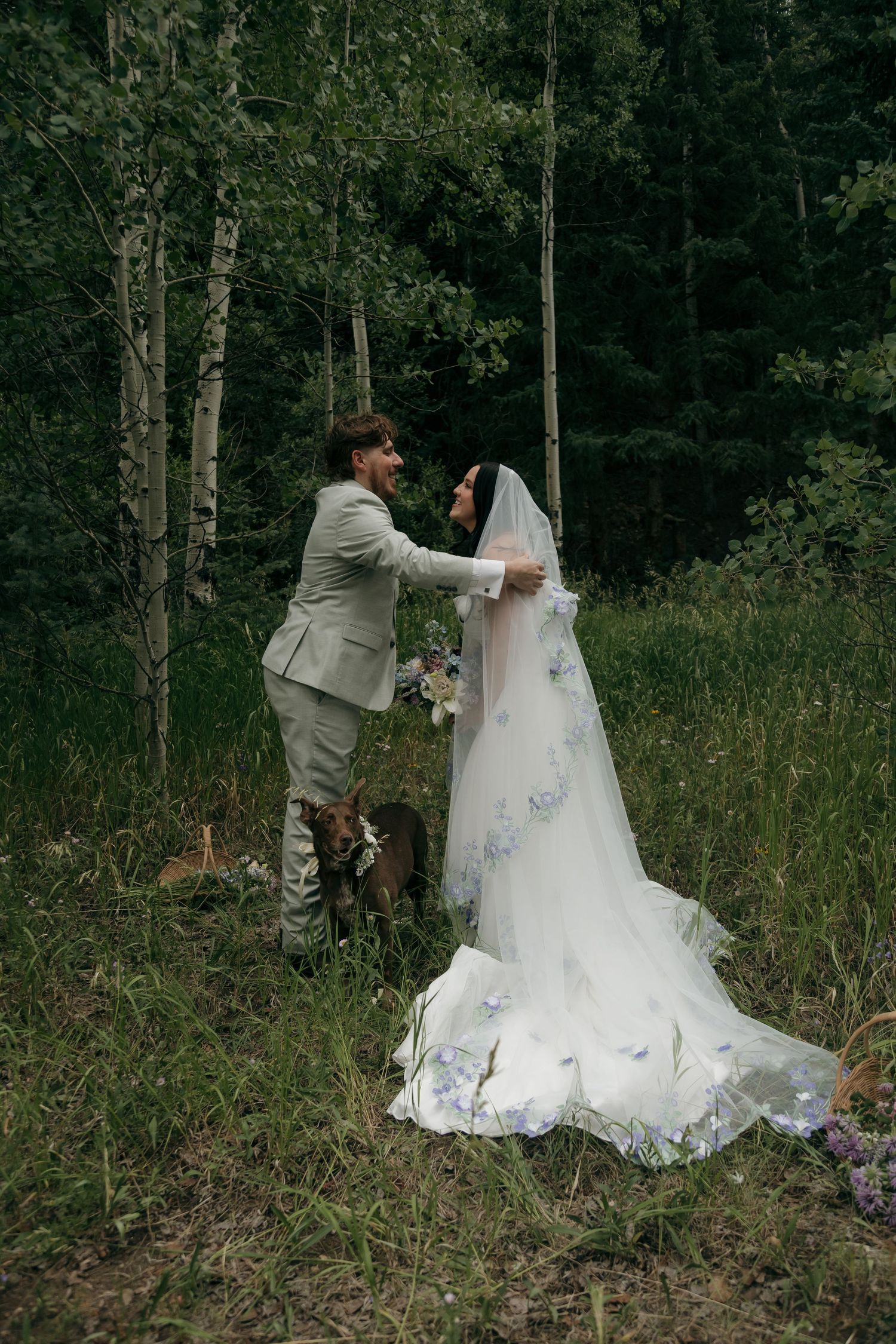 Bride and groom share a romantic moment in a lush forest, bride wearing a floral-embroidered veil and gown.