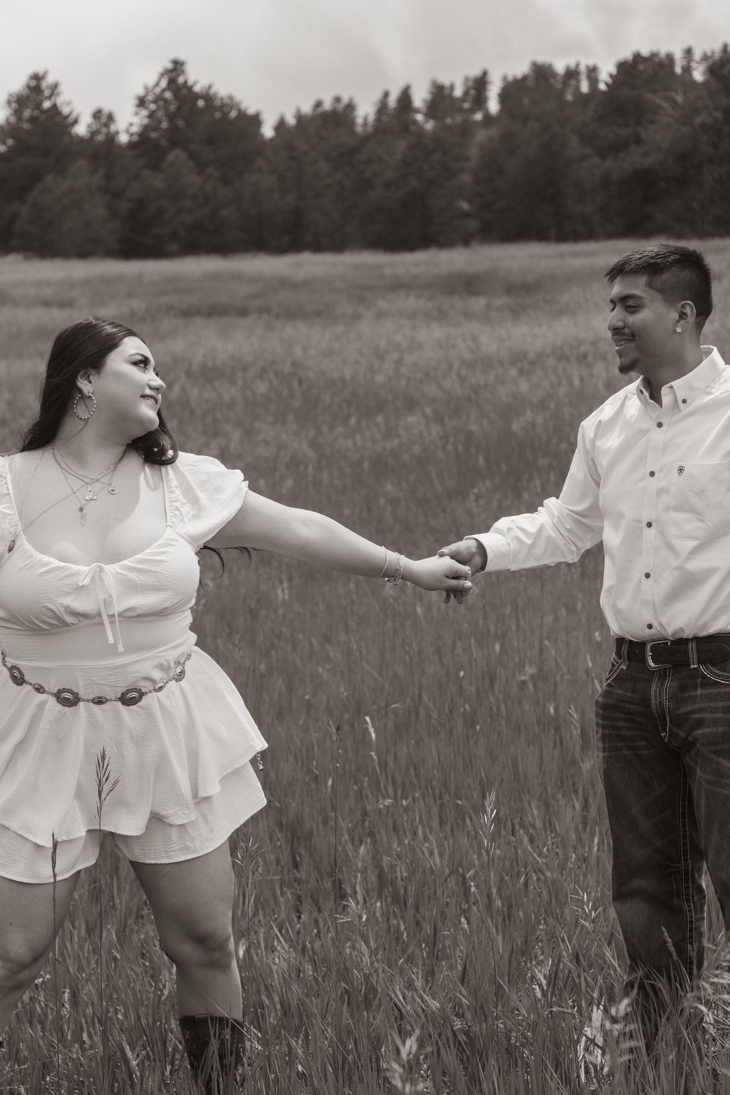 Couple holding hands and running playfully through a tall grass field at sunset.